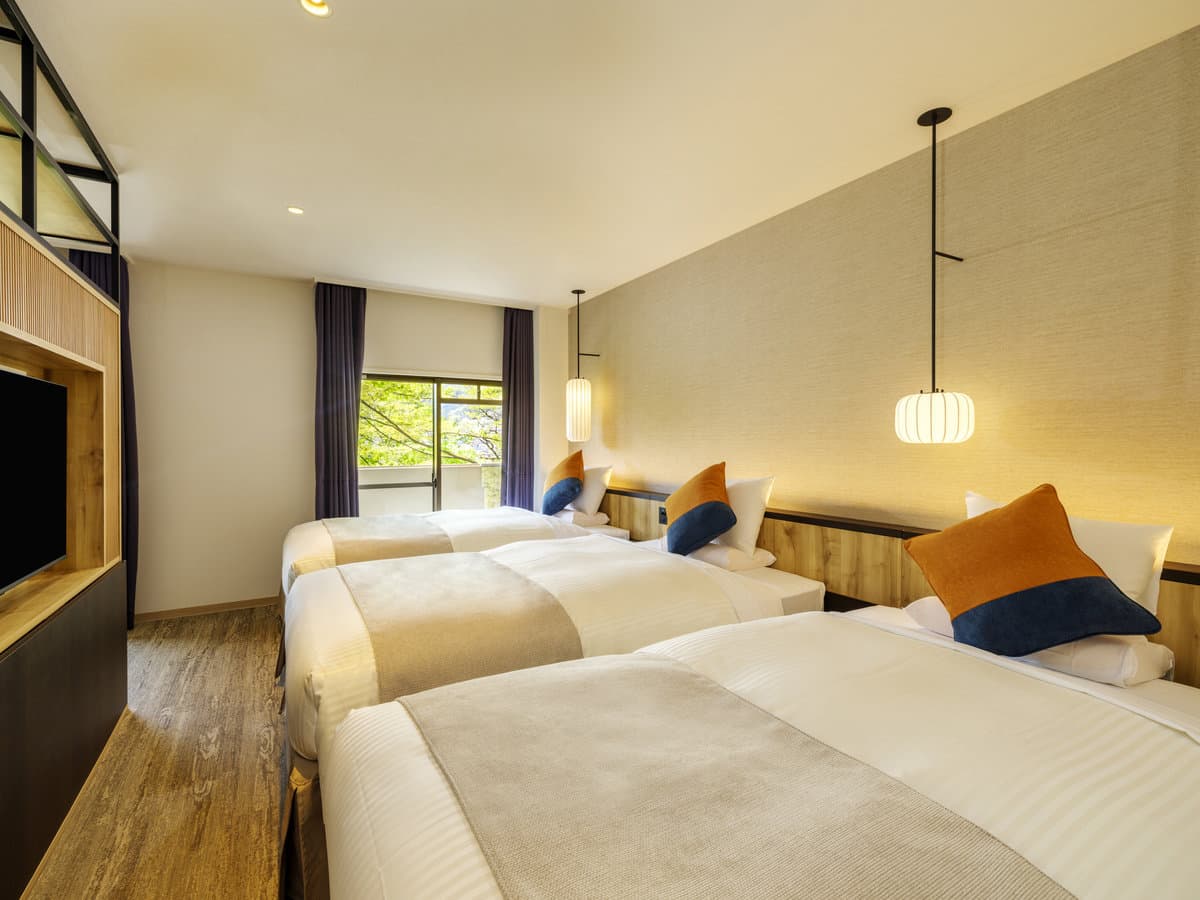 Renovated guest room with twin beds, paper lantern lights and a window framing green hills