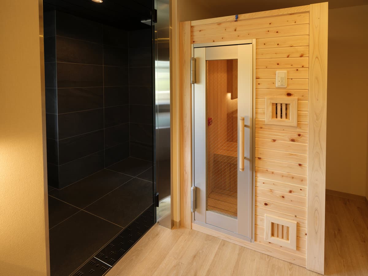 Private in-room dry sauna cabin in natural cedar beside a black-tiled shower area