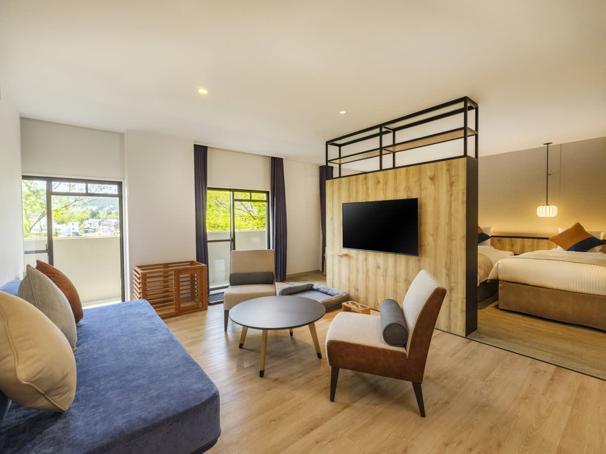 Bright modern suite with living area, sofa bed, low table and a separate bedroom in warm wood tones