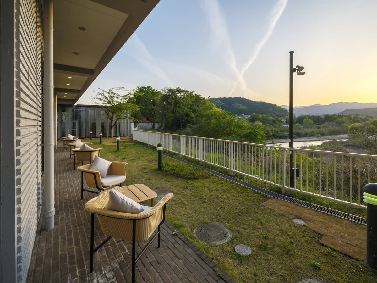 Garden terrace lounge with woven armchairs overlooking the Tama River valley at golden hour