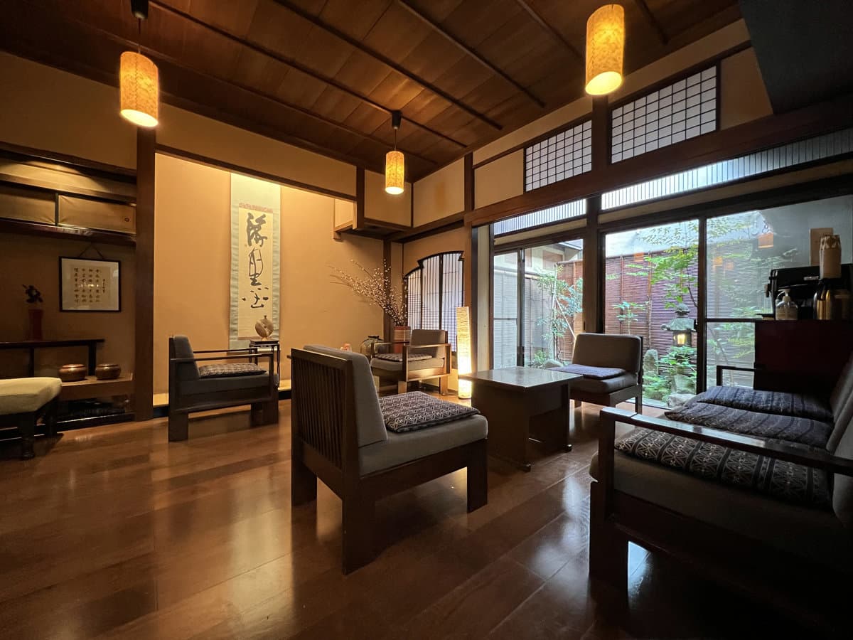 Warmly lit wooden lounge with armchairs, calligraphy scroll and garden view at Ryokan Tanabe in Takayama