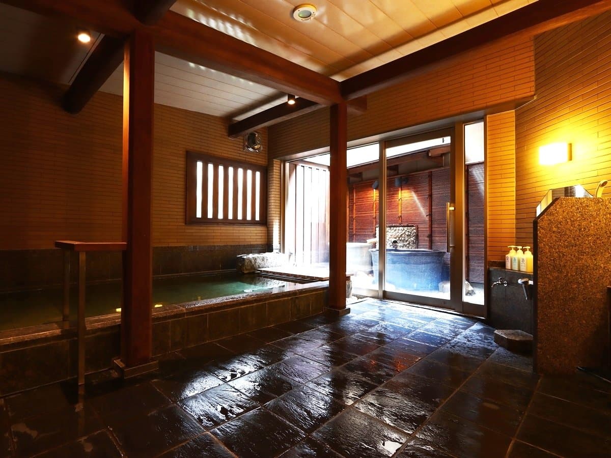 Indoor hot spring bath with stone floor opening onto an outdoor rotenburo at Ryokan Tanabe