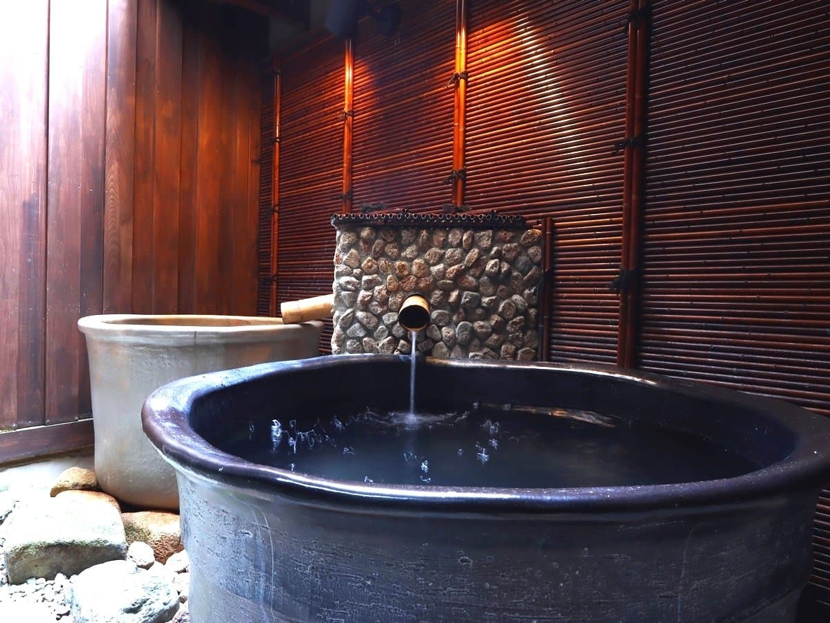 Private ceramic jar bath fed by a bamboo spout beside a wooden lattice screen at Ryokan Tanabe