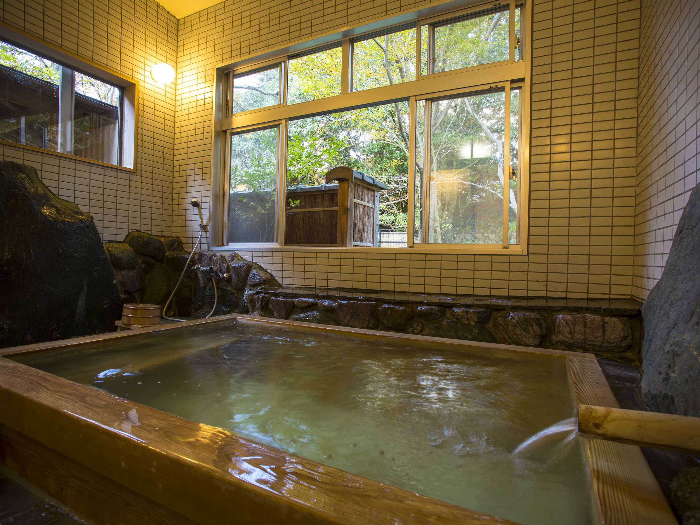 Indoor cypress kinsen bath at Hashinoya Bekkan Ransui in a tiled bathroom with a wooden tub, dipper bucket and a window looking onto the maple garden
