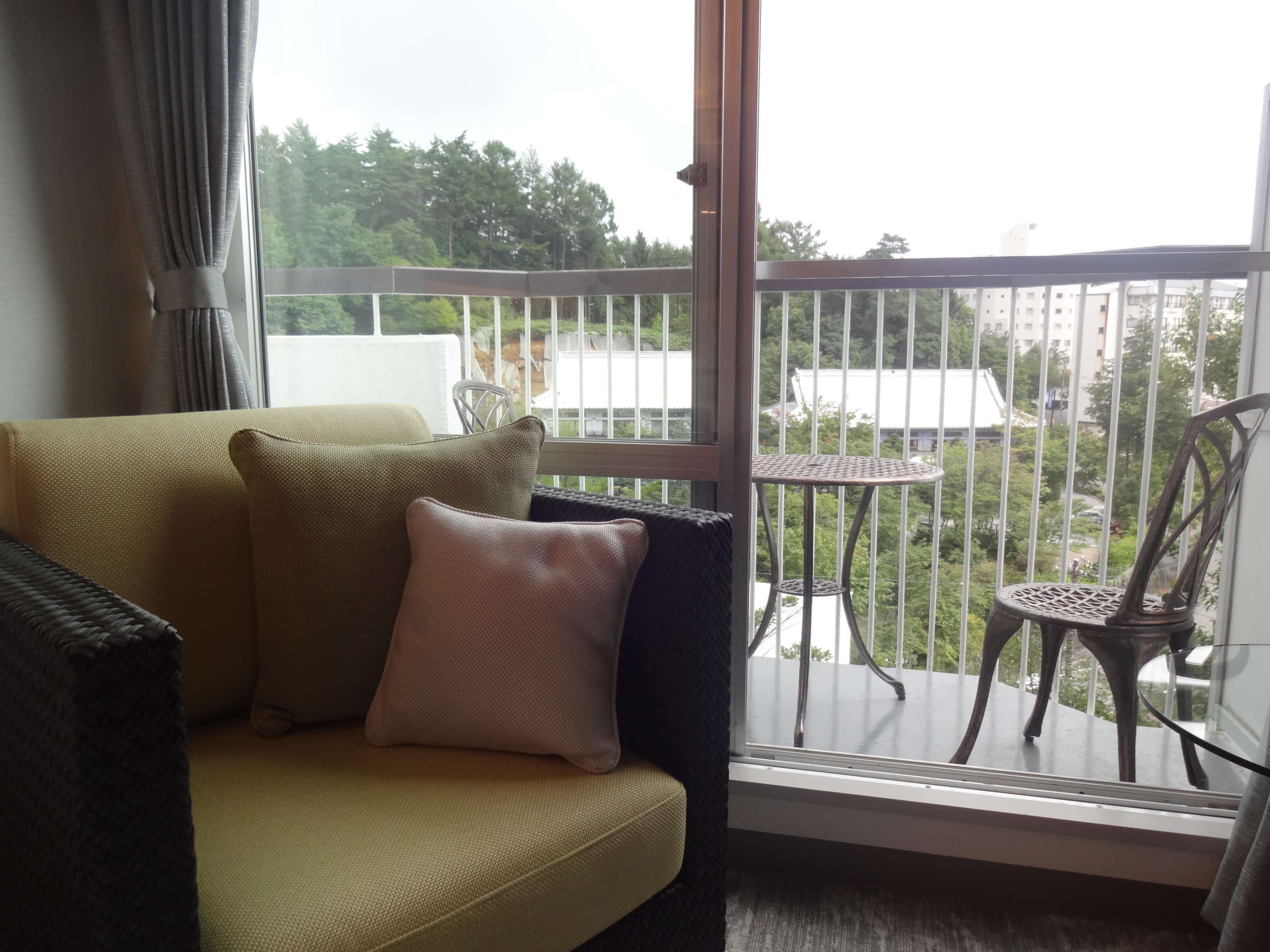 Guest room corner sofa beside a glass balcony with iron cafe chairs overlooking the Kusatsu hot spring town at Hotel Spax Kusatsu