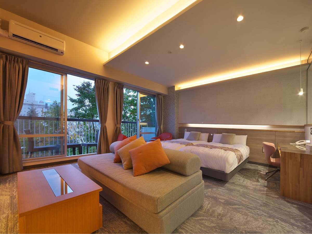 Spacious modern twin-bed guest room with daybed sofa and floor-to-ceiling windows overlooking the town at Hotel Spax Kusatsu
