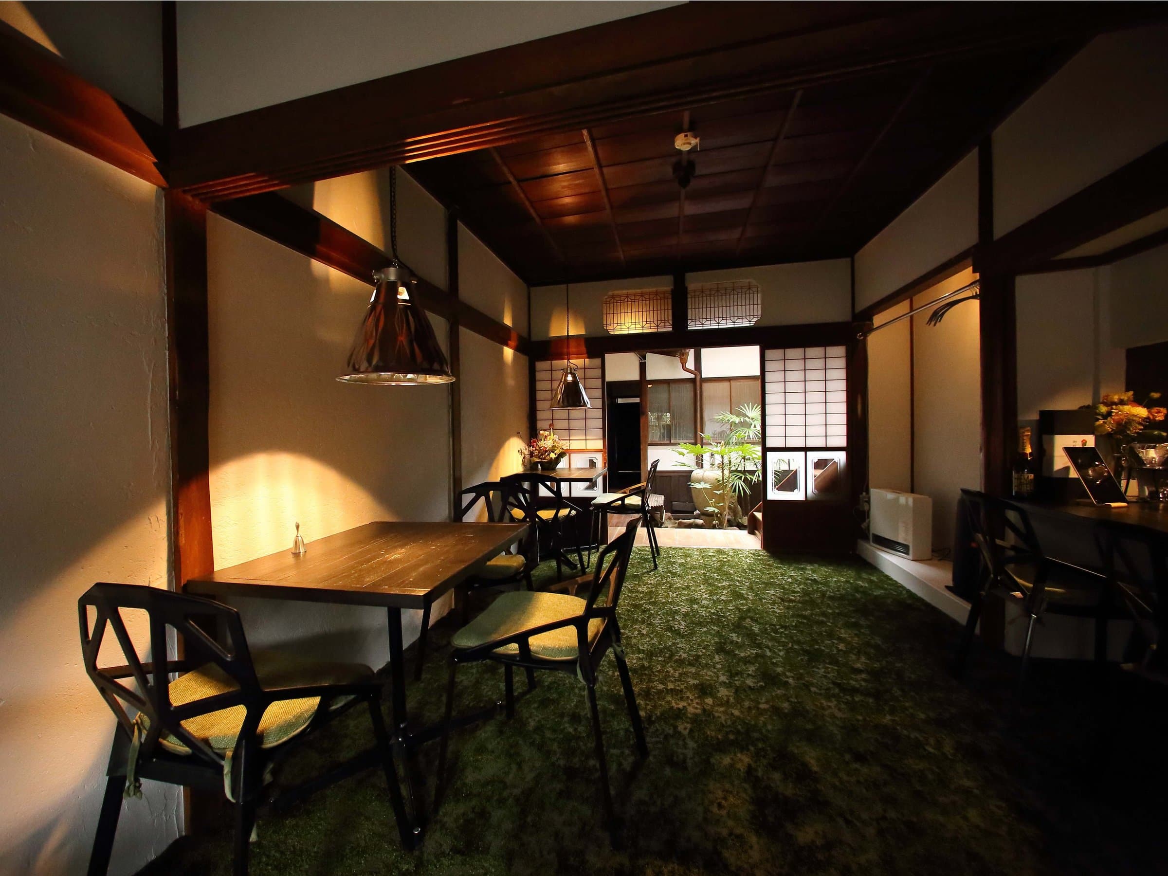 Dining lounge with wooden table, designer chairs, moss-green carpet and pendant lights at Hem's Hotel, Miyajima
