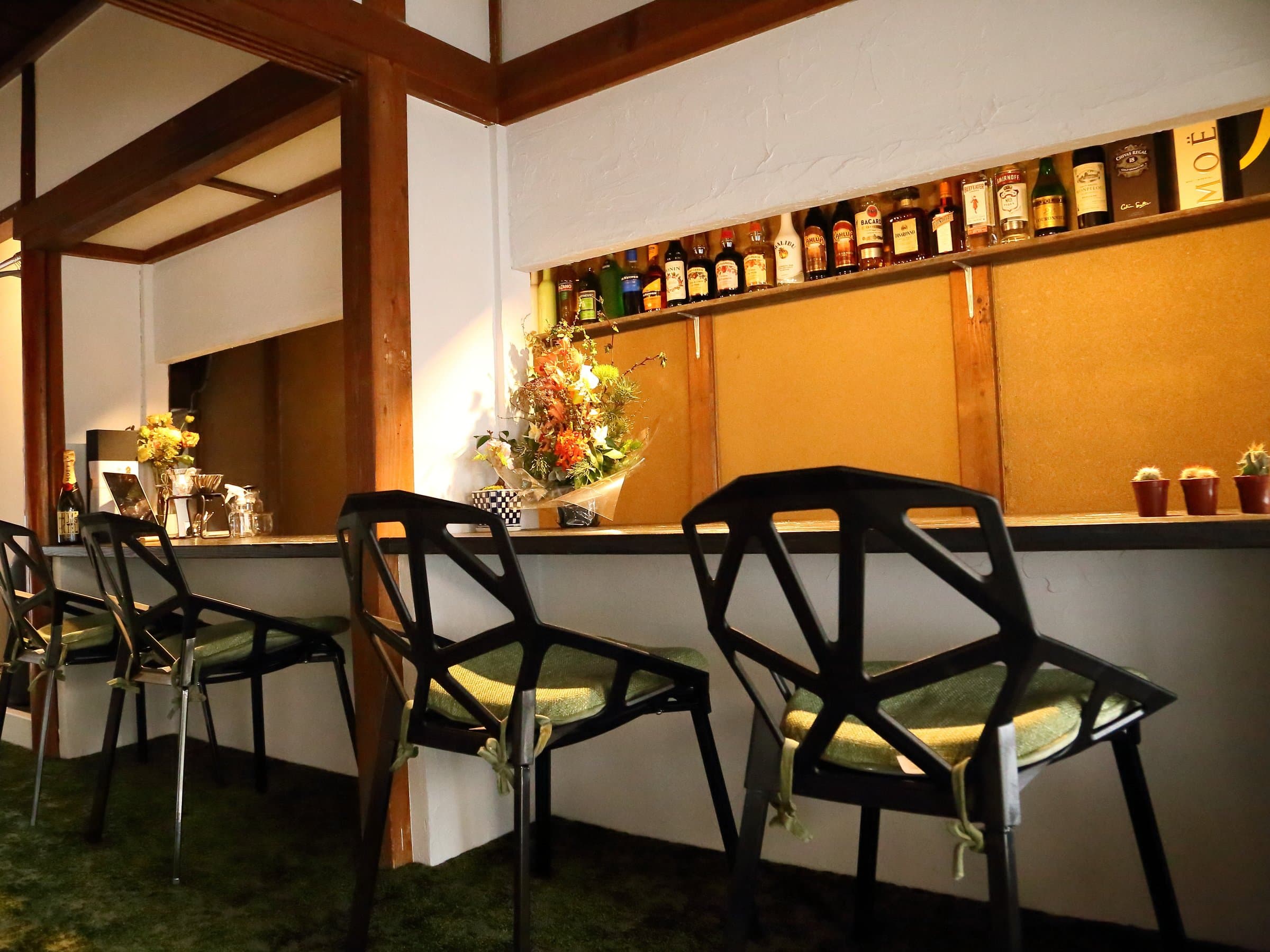 Lounge bar counter lined with bottles and designer chairs over green carpet at Hem's Hotel, Miyajima