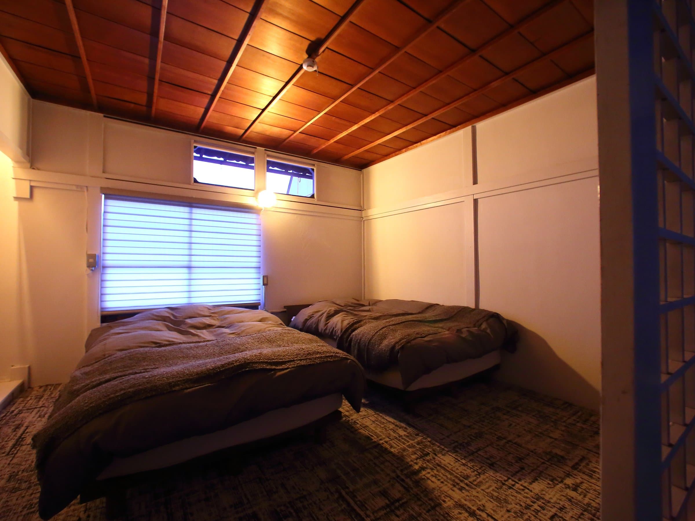Guest bedroom with two low futon beds, wood-plank ceiling and shoji-screened window at Hem's Hotel, Miyajima