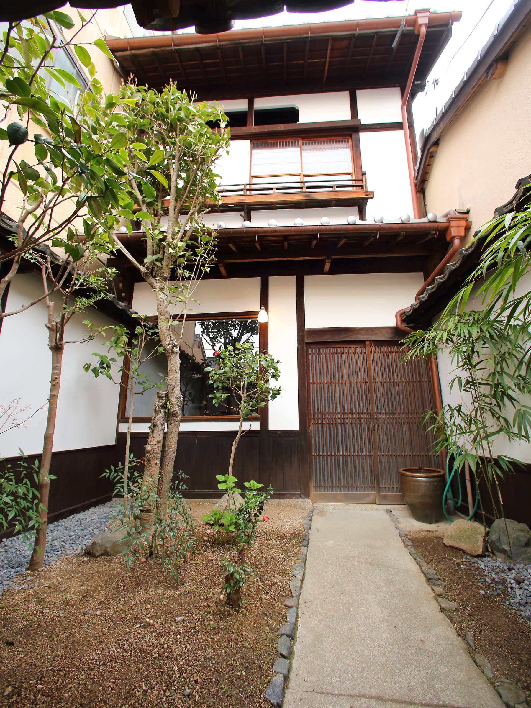 Inner garden courtyard with stepping-stone path and shrubs framing the two-story machiya facade at Hem's Hotel, Miyajima