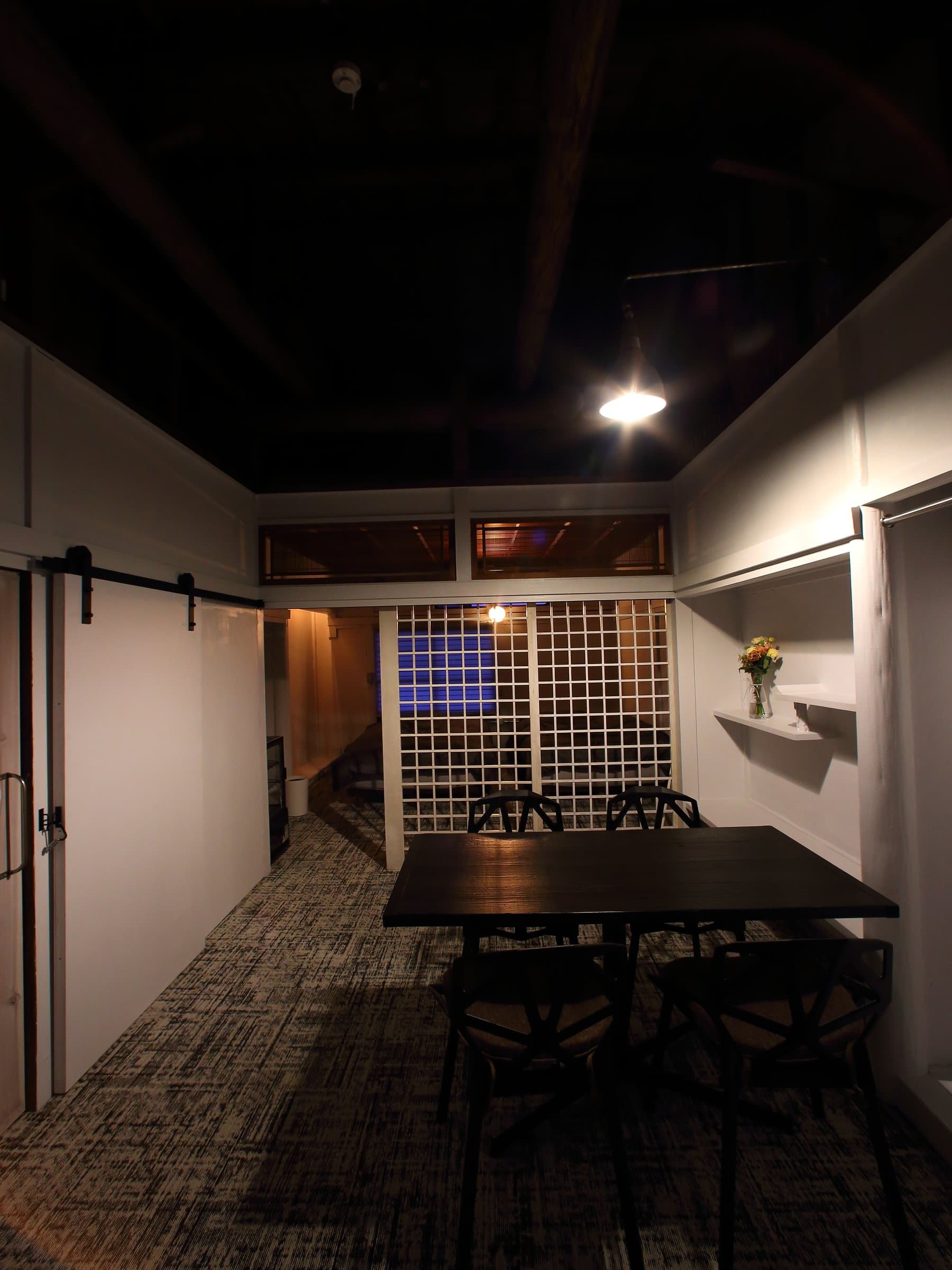 Open-plan living and dining space with exposed high beams, lattice partition and dining table at Hem's Hotel, Miyajima