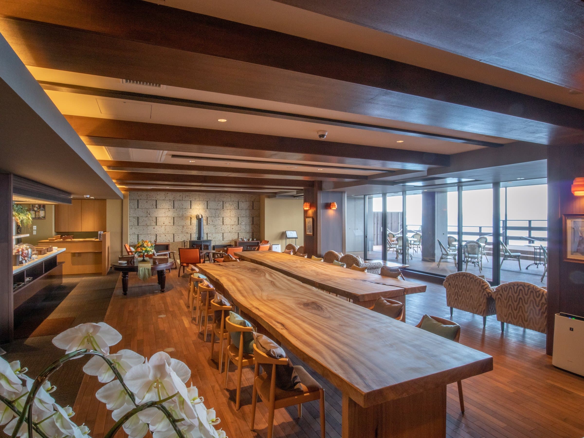 Lounge with long live-edge wood communal table, woven chairs and ocean view through full-height windows, Amane Resort GAHAMA, Beppu Onsen