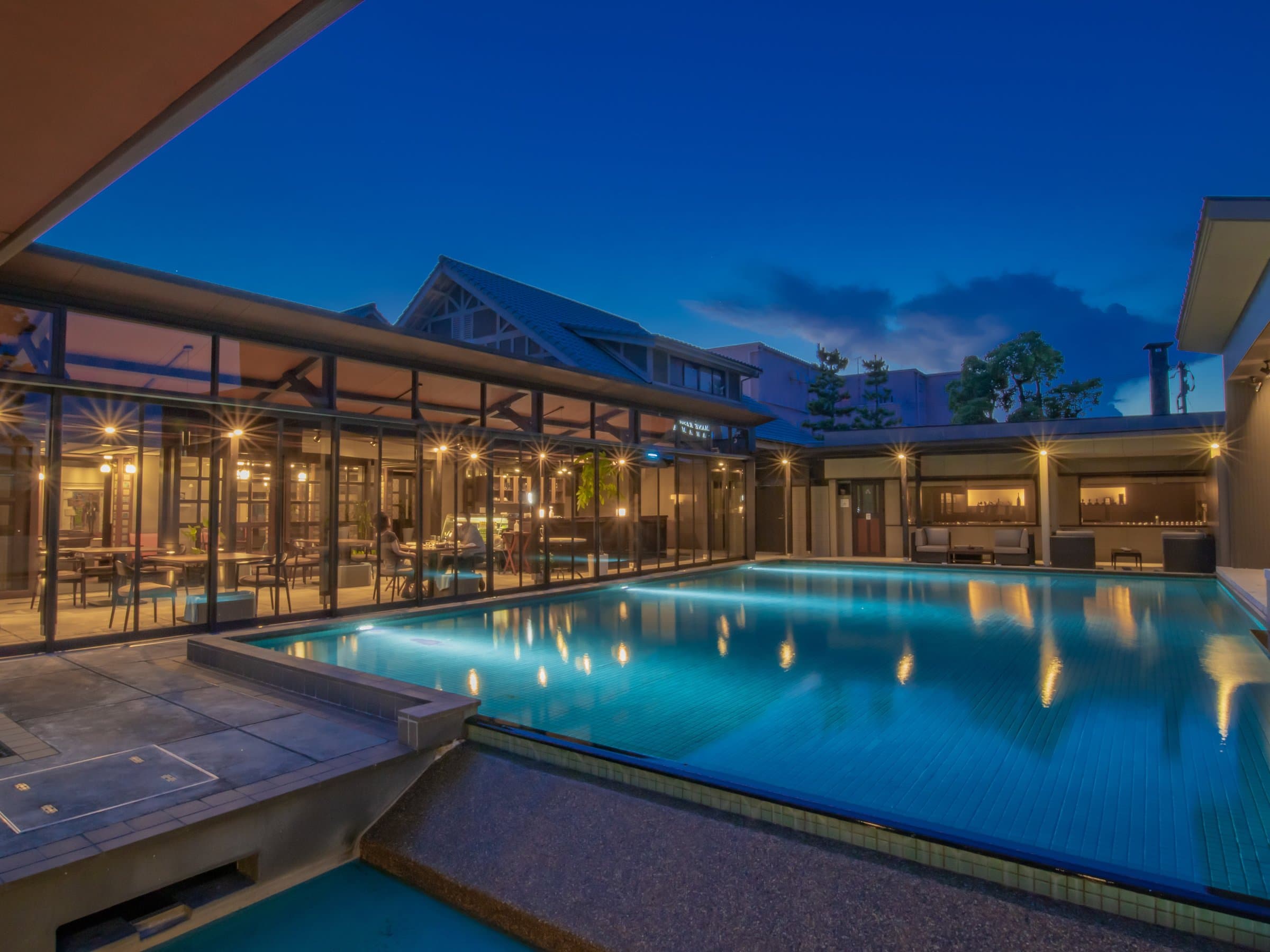Illuminated courtyard pool at dusk reflecting a glass-walled lounge under deep blue evening sky, Amane Resort GAHAMA, Beppu Onsen
