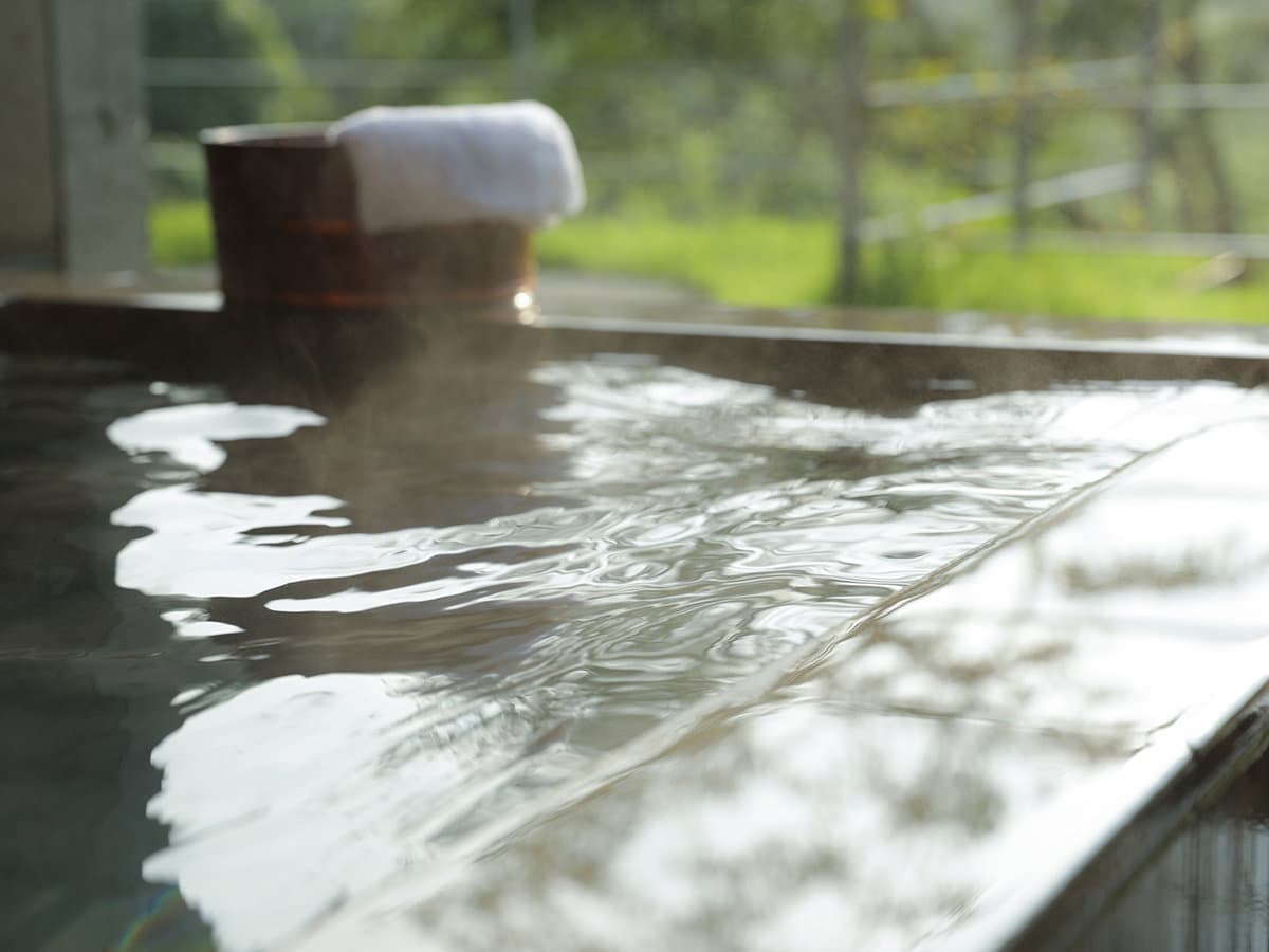 Steaming hot-spring bath water with a copper pail and towel beside a forest view at Sanso Warabino