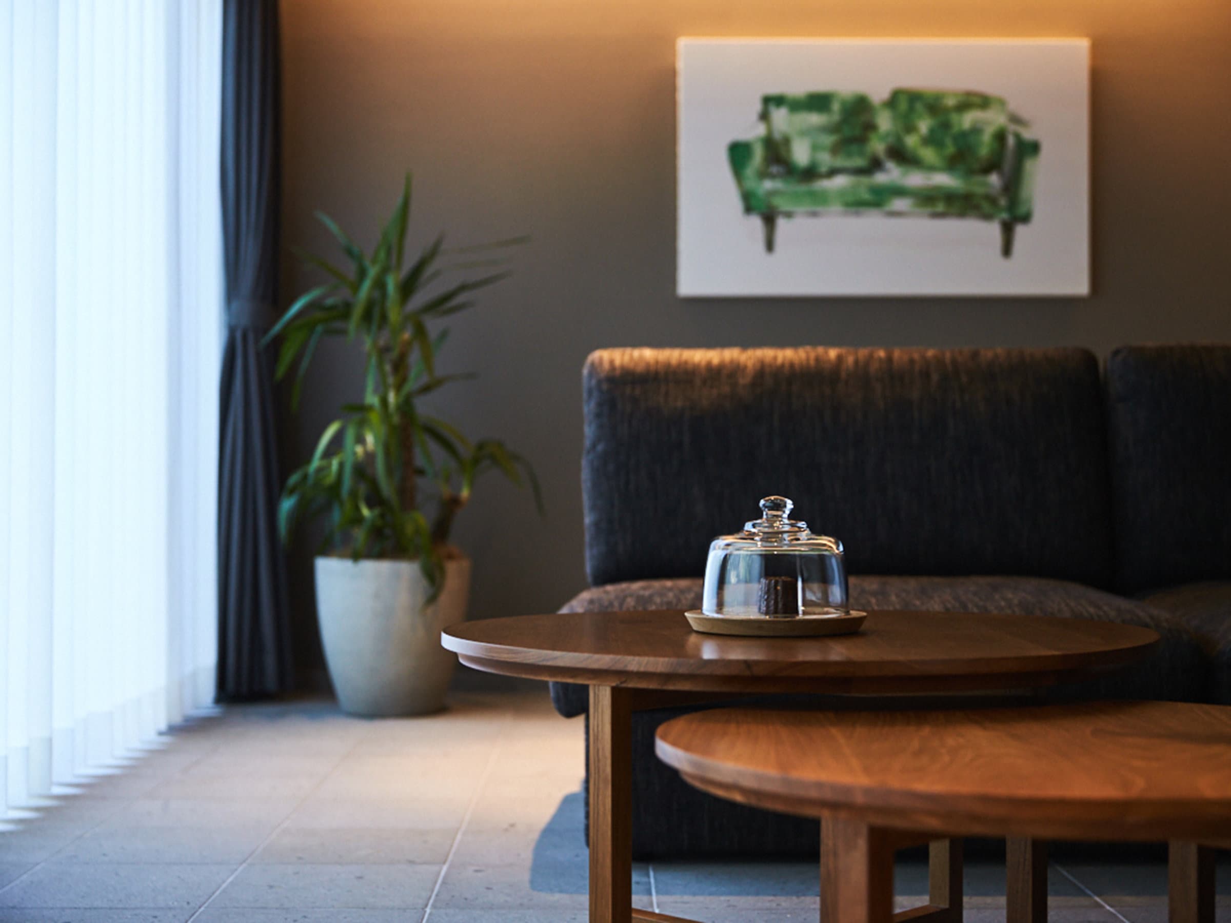 Guest room sitting area at Sanso Warabino with a charcoal sofa, walnut tables and framed artwork