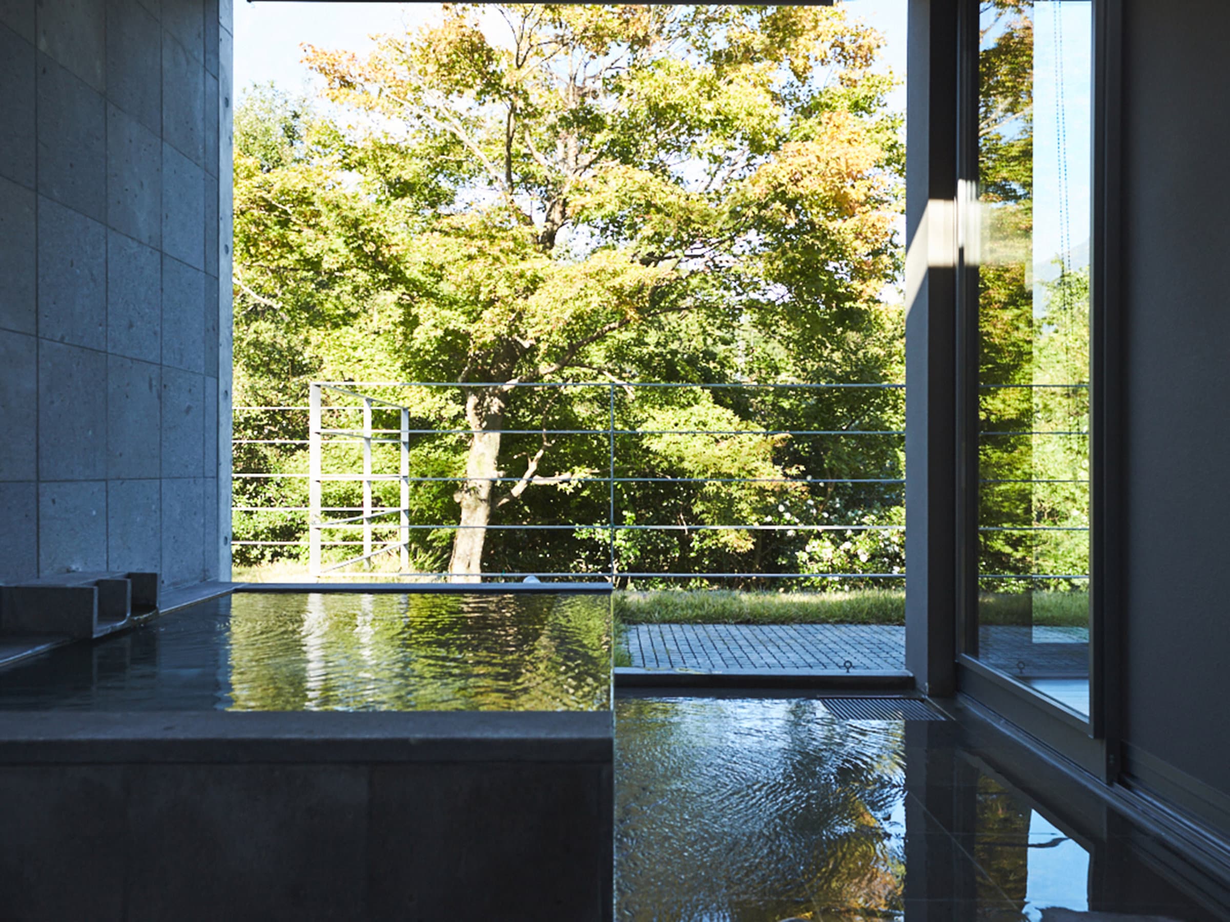 Indoor stone onsen bath at Sanso Warabino with full-height glass overlooking a green Yufuin forest