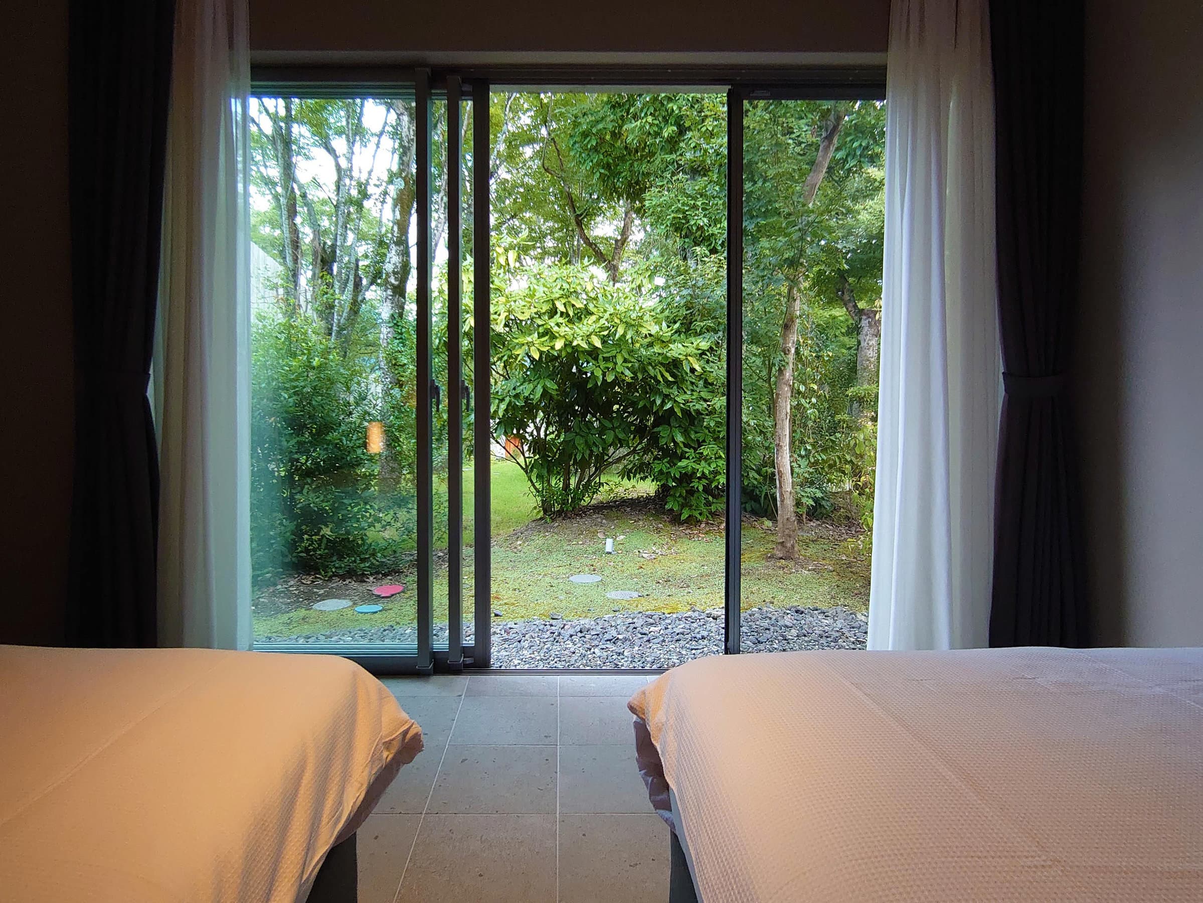Guest room with twin beds at Sanso Warabino opening onto a private green garden through floor-to-ceiling glass