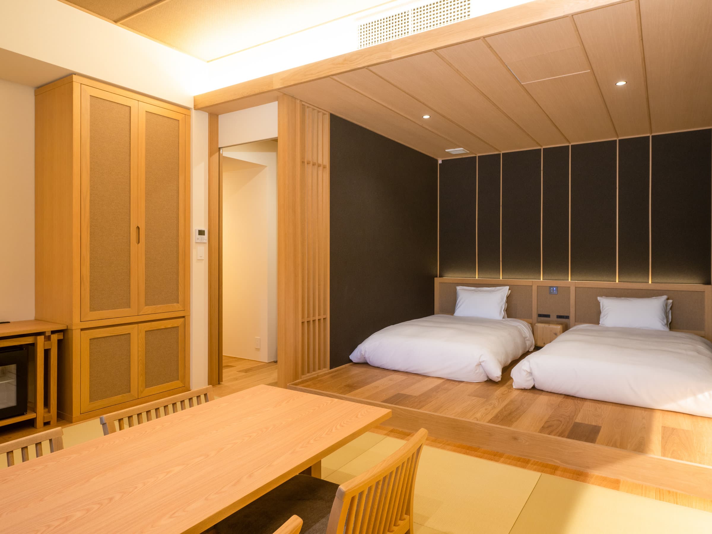 Contemporary Japanese guest room with twin low beds on a raised wooden platform and a dining table