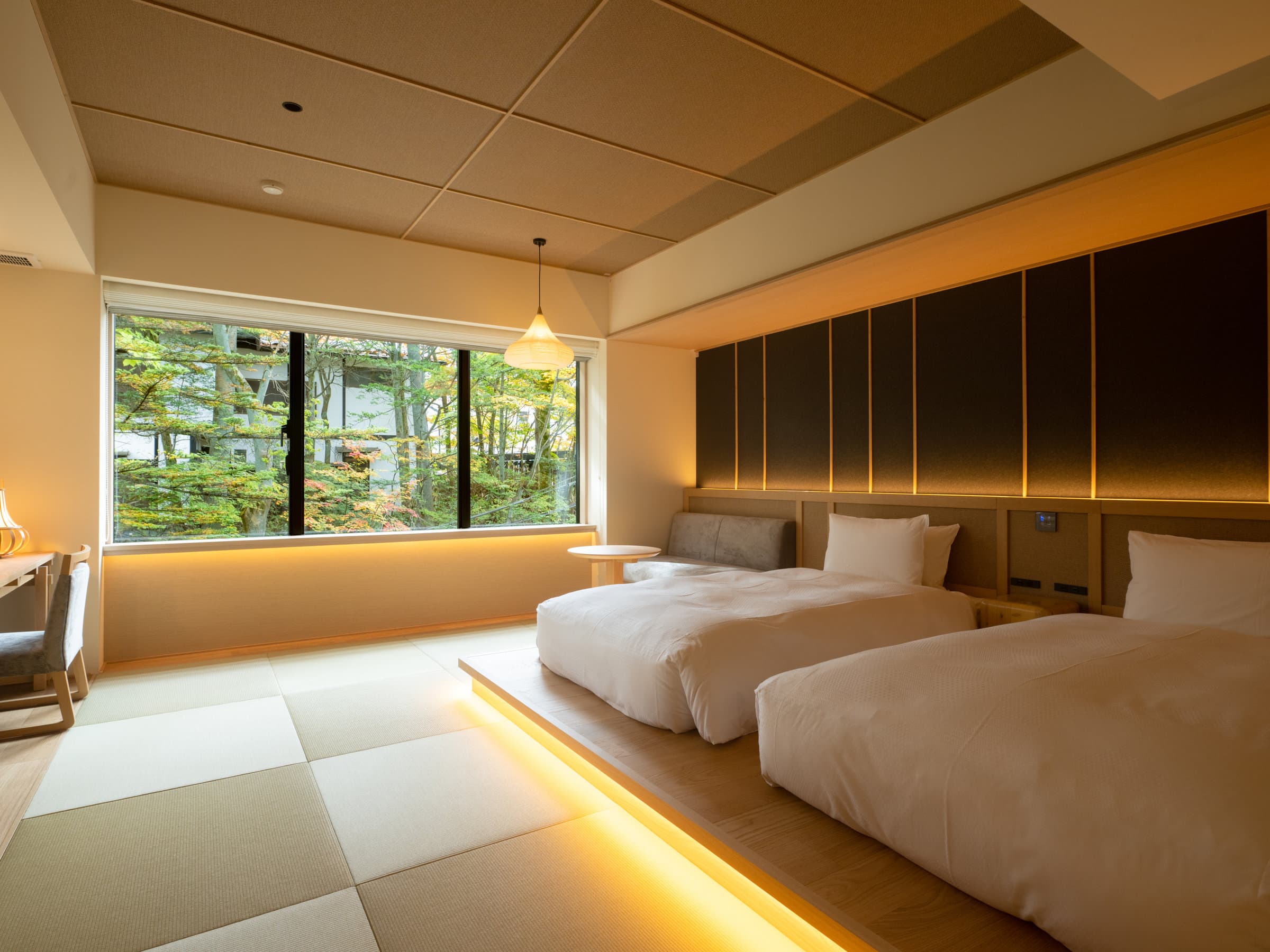 Warmly lit twin-bed room with floor lighting and a large window overlooking green forest