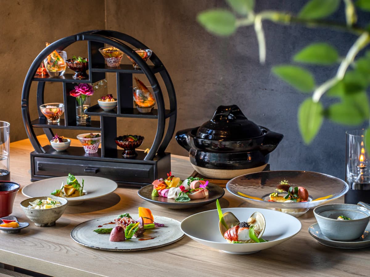 Multi-course kaiseki dinner of small plates, a tiered stand and a black clay pot on a wooden table