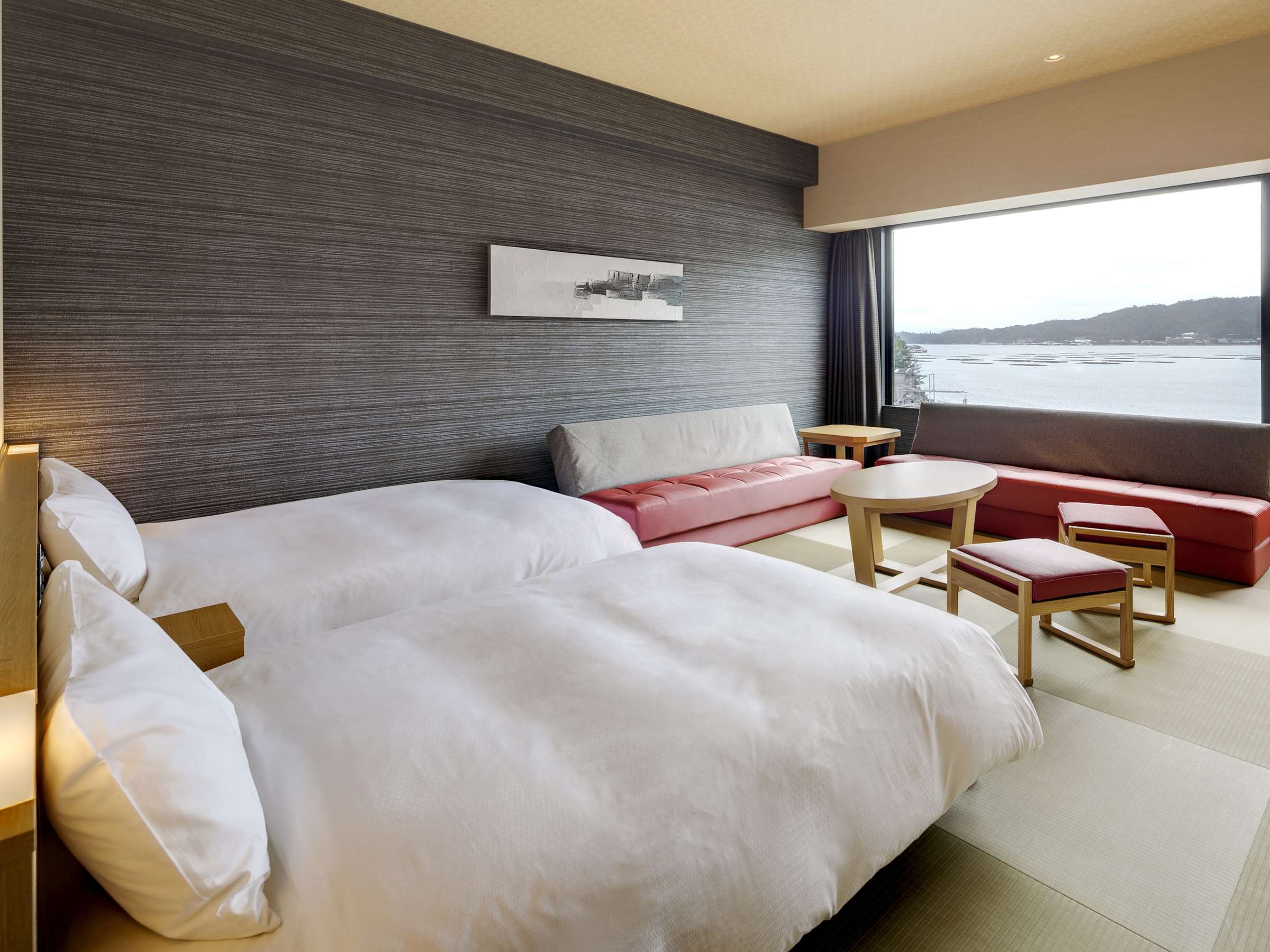 Deluxe twin room with grey textile wall, low red sofa seating and panoramic sea-view window