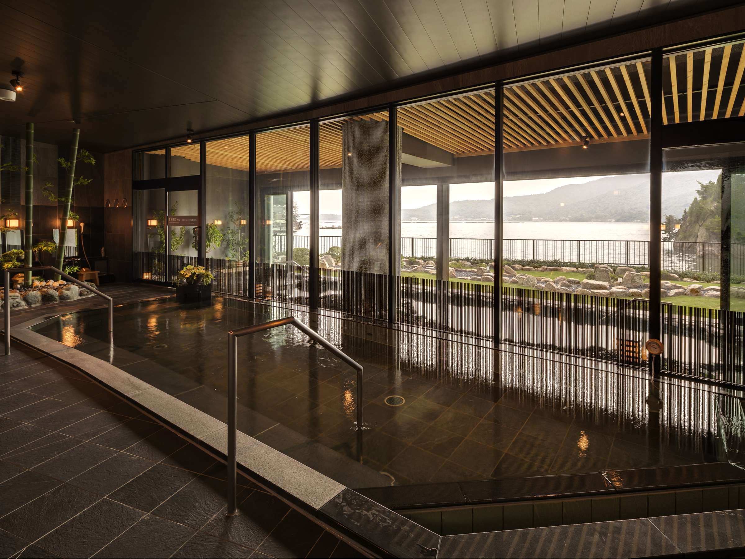 Indoor onsen bath with stone surround and floor-to-ceiling glass overlooking the Seto Inland Sea