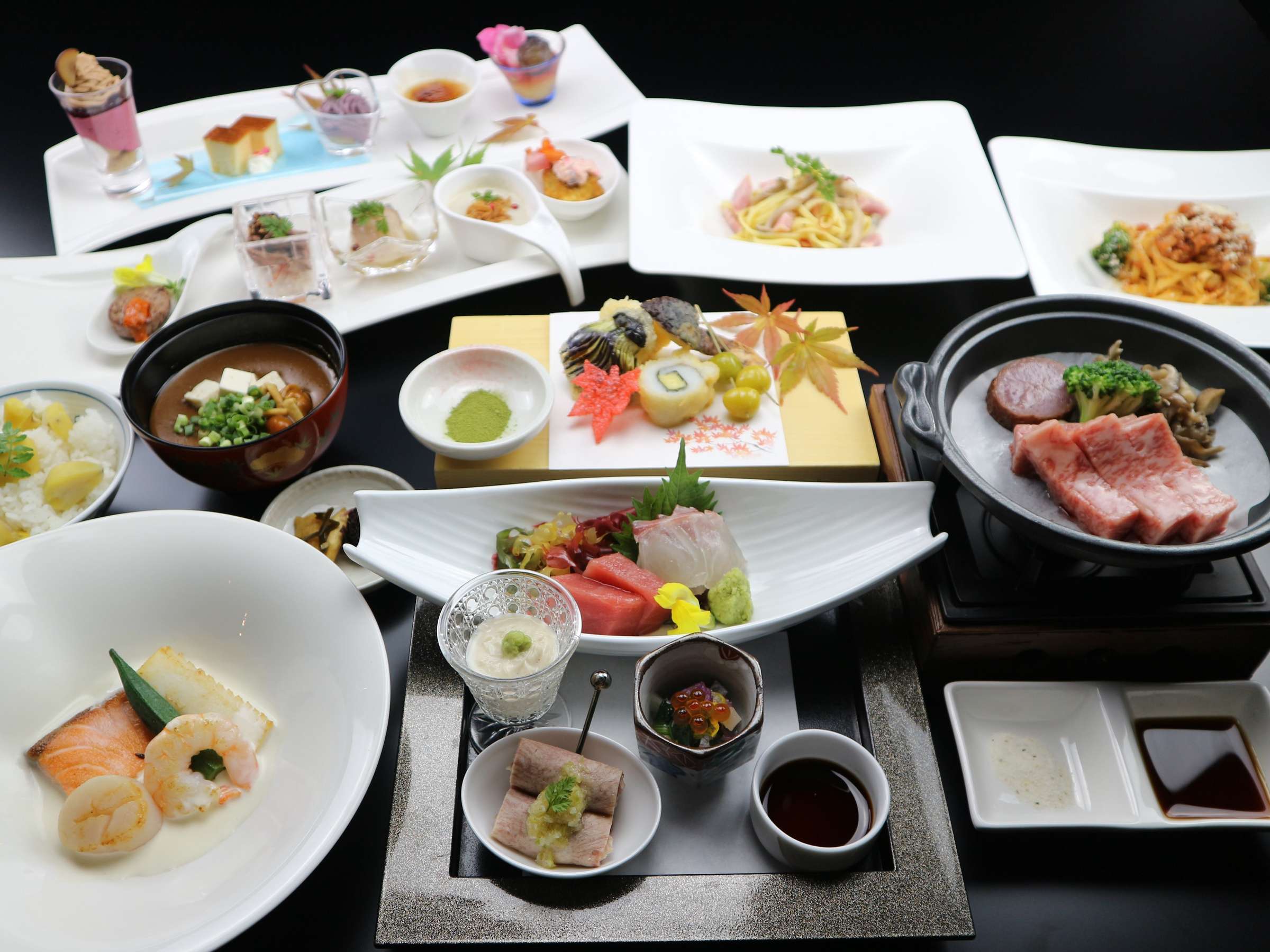 Multi-course Japanese kaiseki dinner spread with sashimi, beef hotpot, soup and small dishes on a dark table