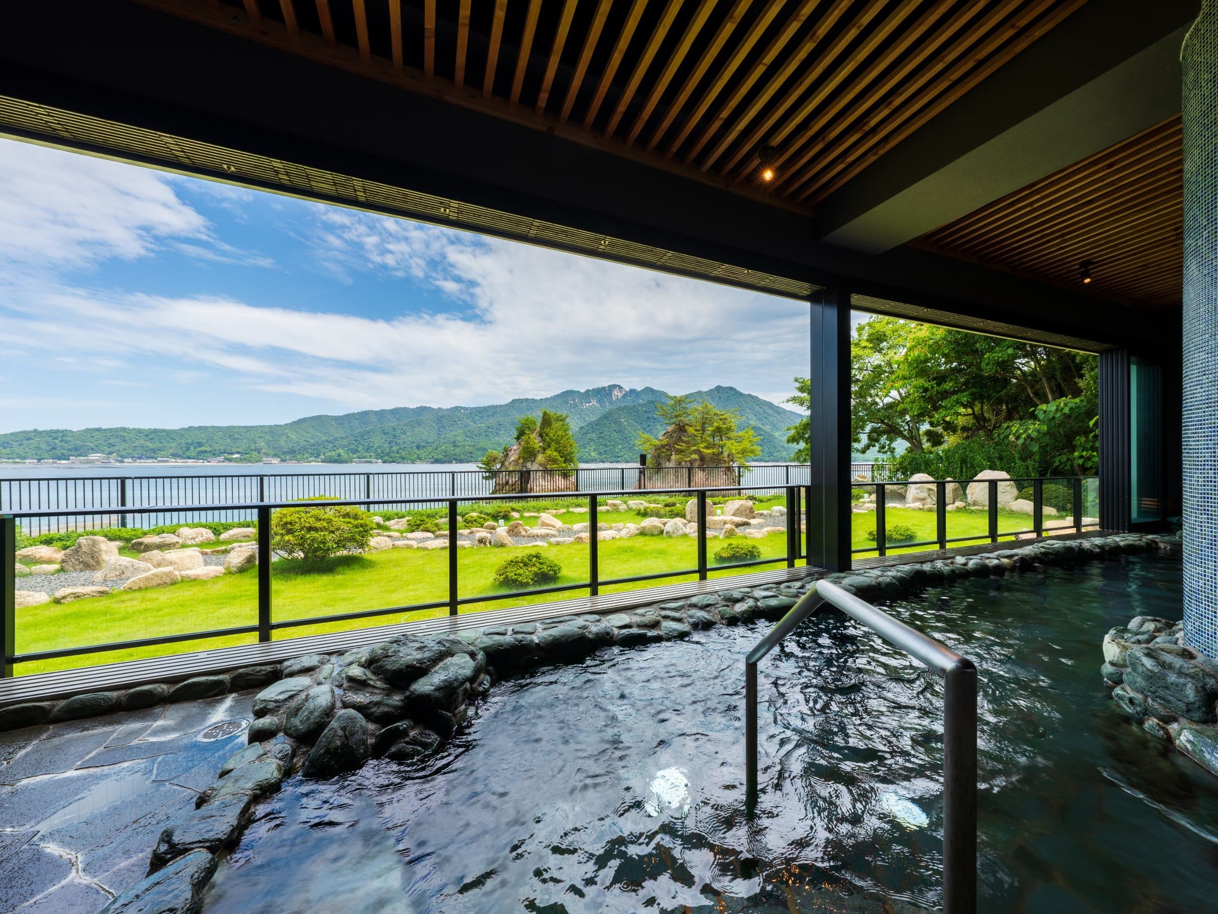 Open-air rotenburo hot spring bath looking out over a garden, the Seto Inland Sea and mountains in daylight