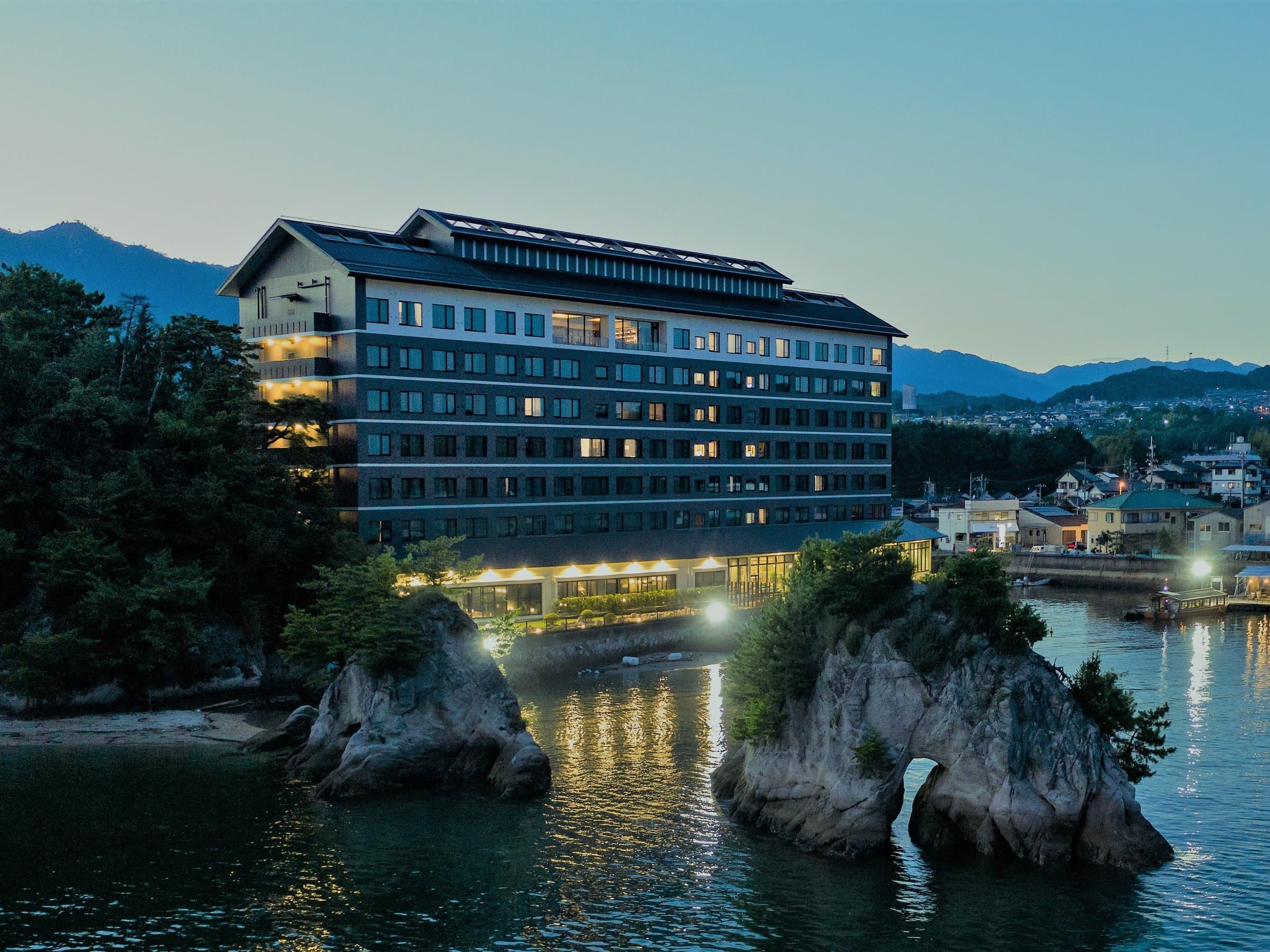 Grandvrio Hotel Miyajima Wakura full seaside exterior lit at dusk above Setouchi inlet rocks near Miyajimaguchi, Hiroshima