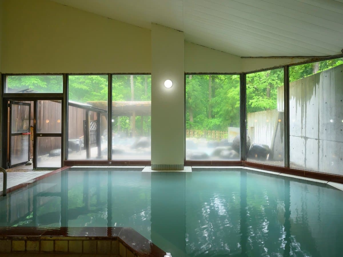 Indoor onsen bath with steaming water and floor-to-ceiling windows facing the forest at Zao Onsen