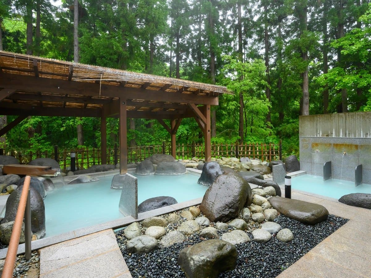 Outdoor hot spring bath with stone garden and surrounding cedar forest at Hotel Waldberg in Zao