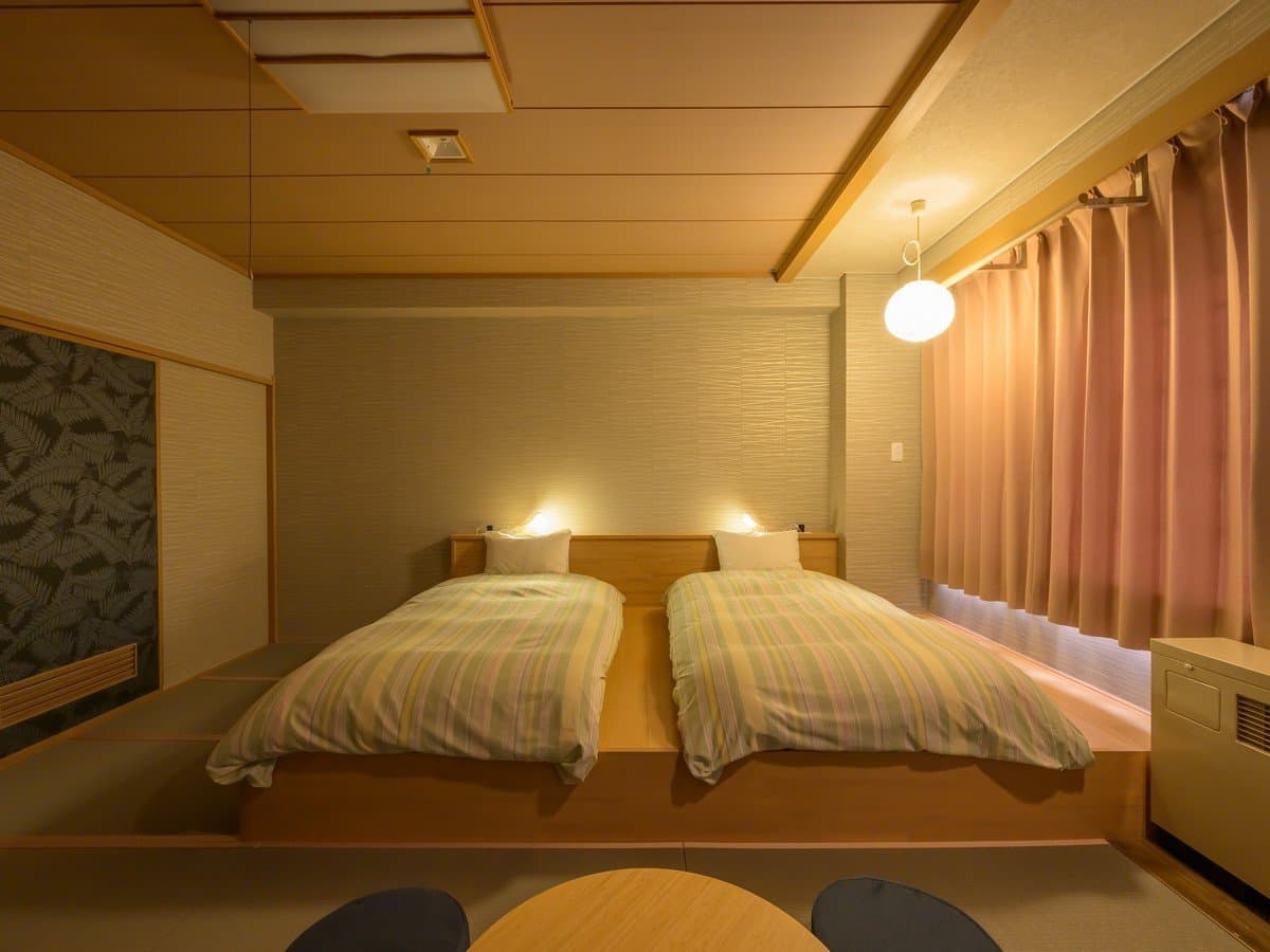 Warmly lit modern Japanese-style guest room with twin low beds on a tatami platform at Hotel Waldberg