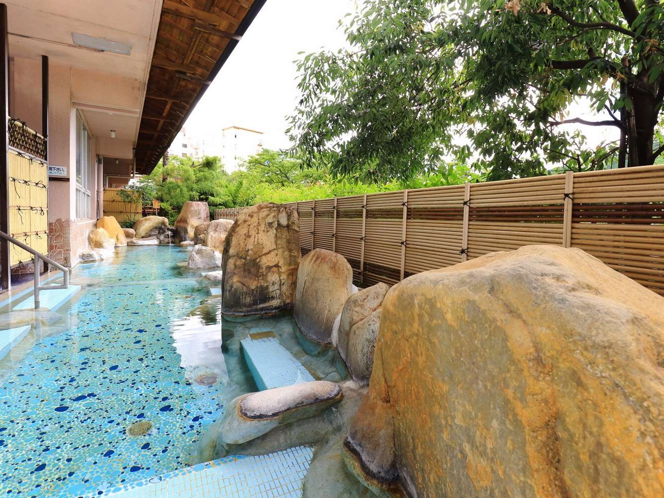 Daytime rotenburo edged with large boulders and bamboo fencing beside greenery, Bosenkan, Gero Onsen