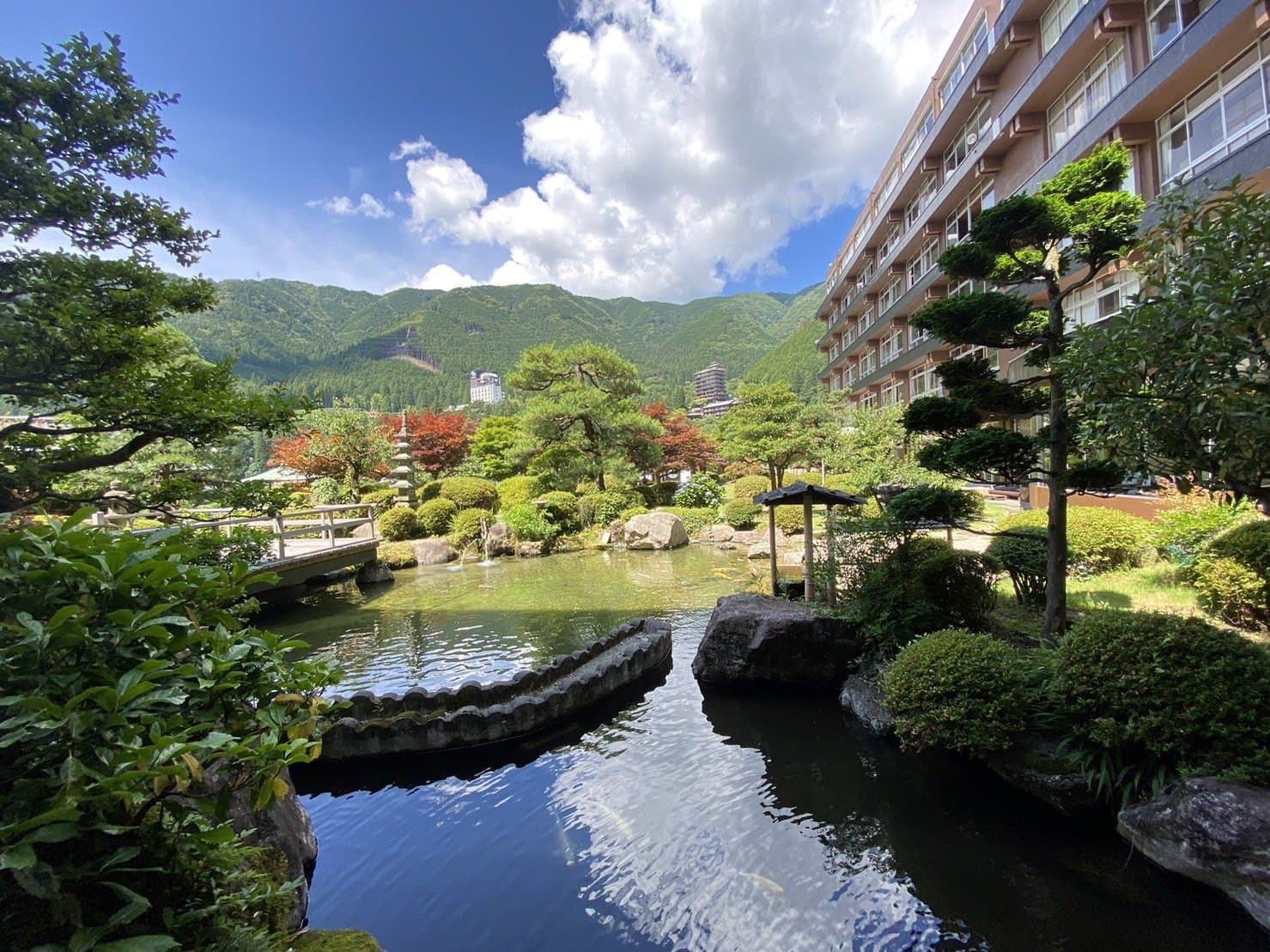 Landscaped Japanese garden with pond and stone bridge before the ryokan building and green mountains, Bosenkan, Gero Onsen