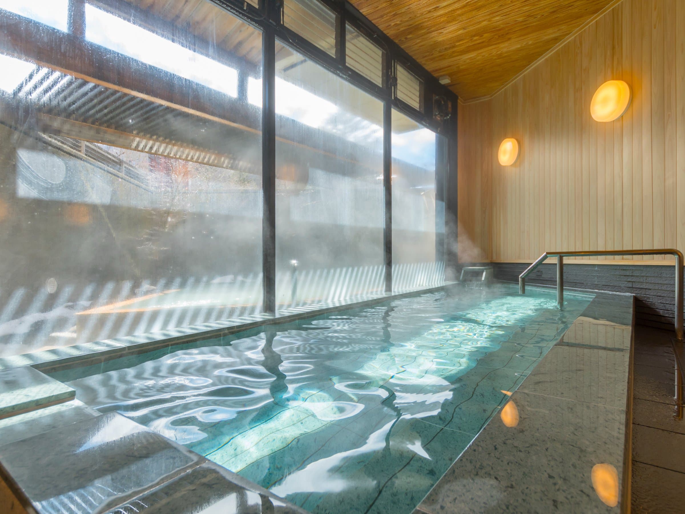 Steaming indoor hot-spring bath with wooden ceiling and tall windows at Hotel Hana-An
