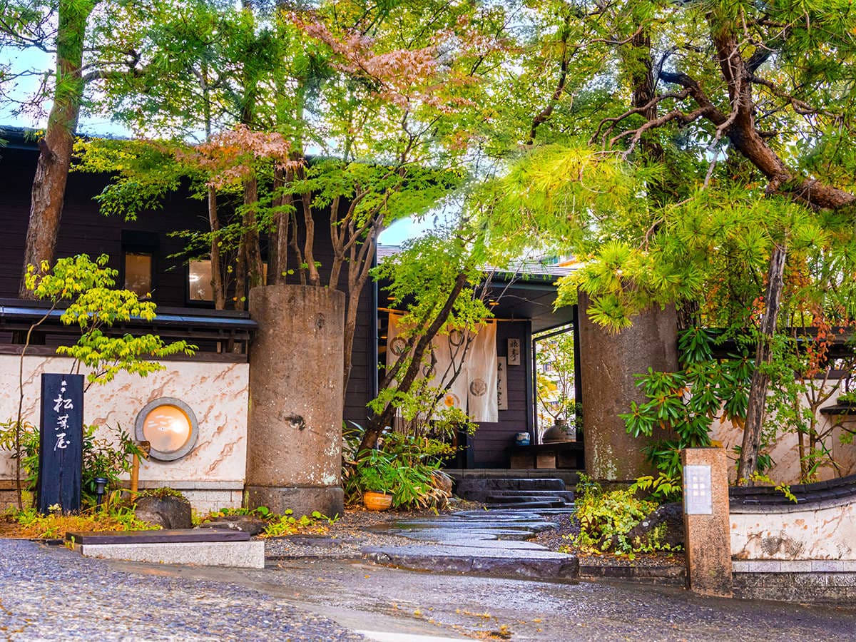 Stone-paved entrance gateway surrounded by lush trees and greenery leading into the traditional inn, Ryotei Matsubaya, Beppu Onsen