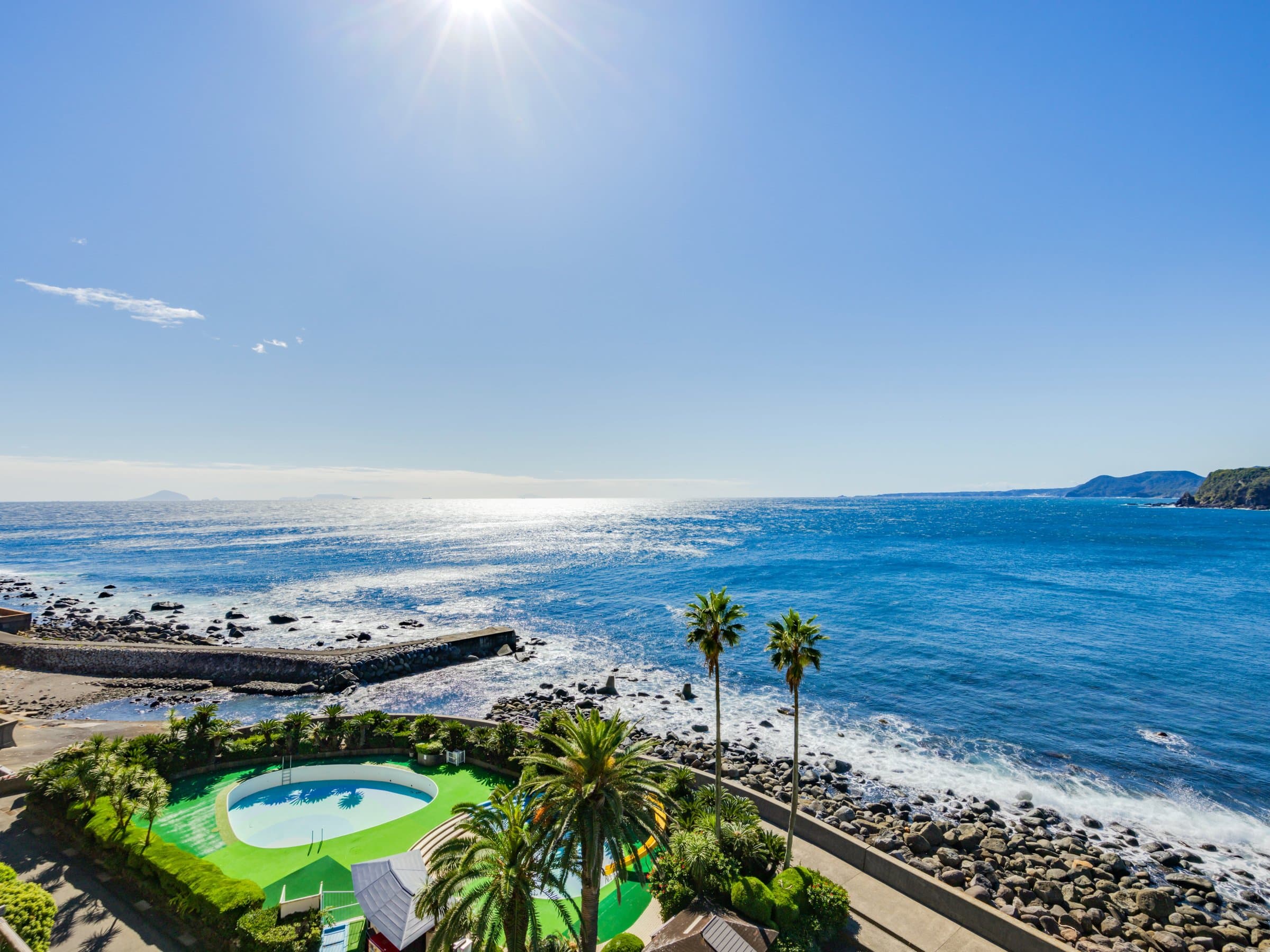 Panoramic Pacific Ocean view over the rocky Izu coastline and garden pool at Inatori Ginsuiso