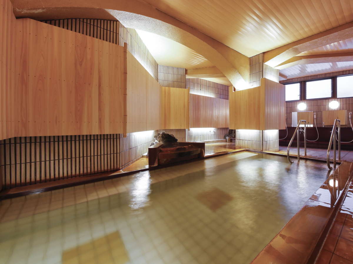Spacious indoor wooden public bath with curved timber ceiling at Hotel Kanichi