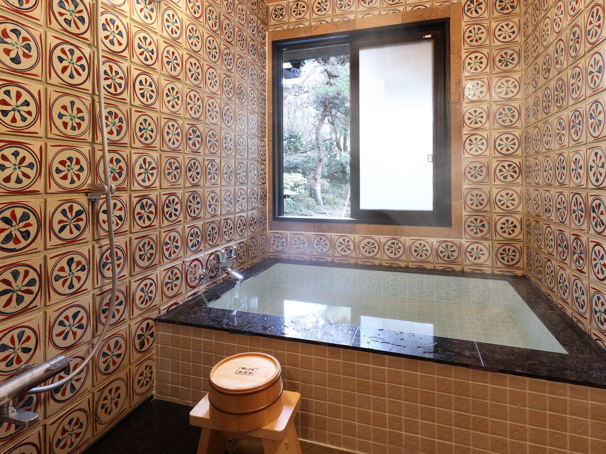 Special-room in-room hot spring bath wrapped in retro patterned tiles beside a garden window, Suimeikan, Gero Onsen