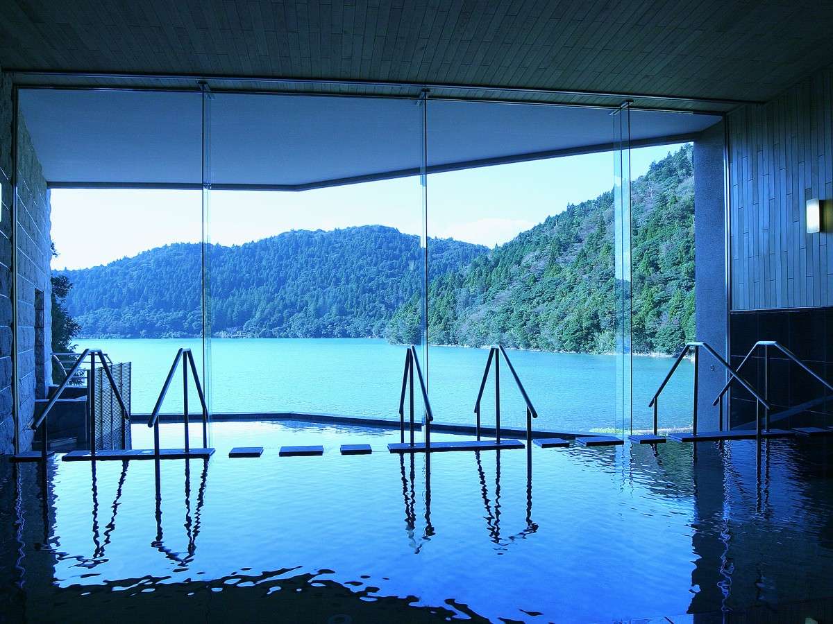 Daytime indoor bath at Unzen Azumaen with panoramic glass windows over the turquoise lake and mountains