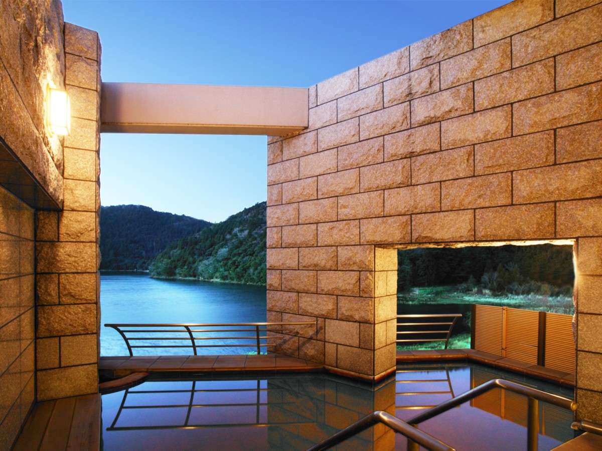 Stone-walled rotenburo at Unzen Azumaen overlooking the lake at dusk in warm twilight light