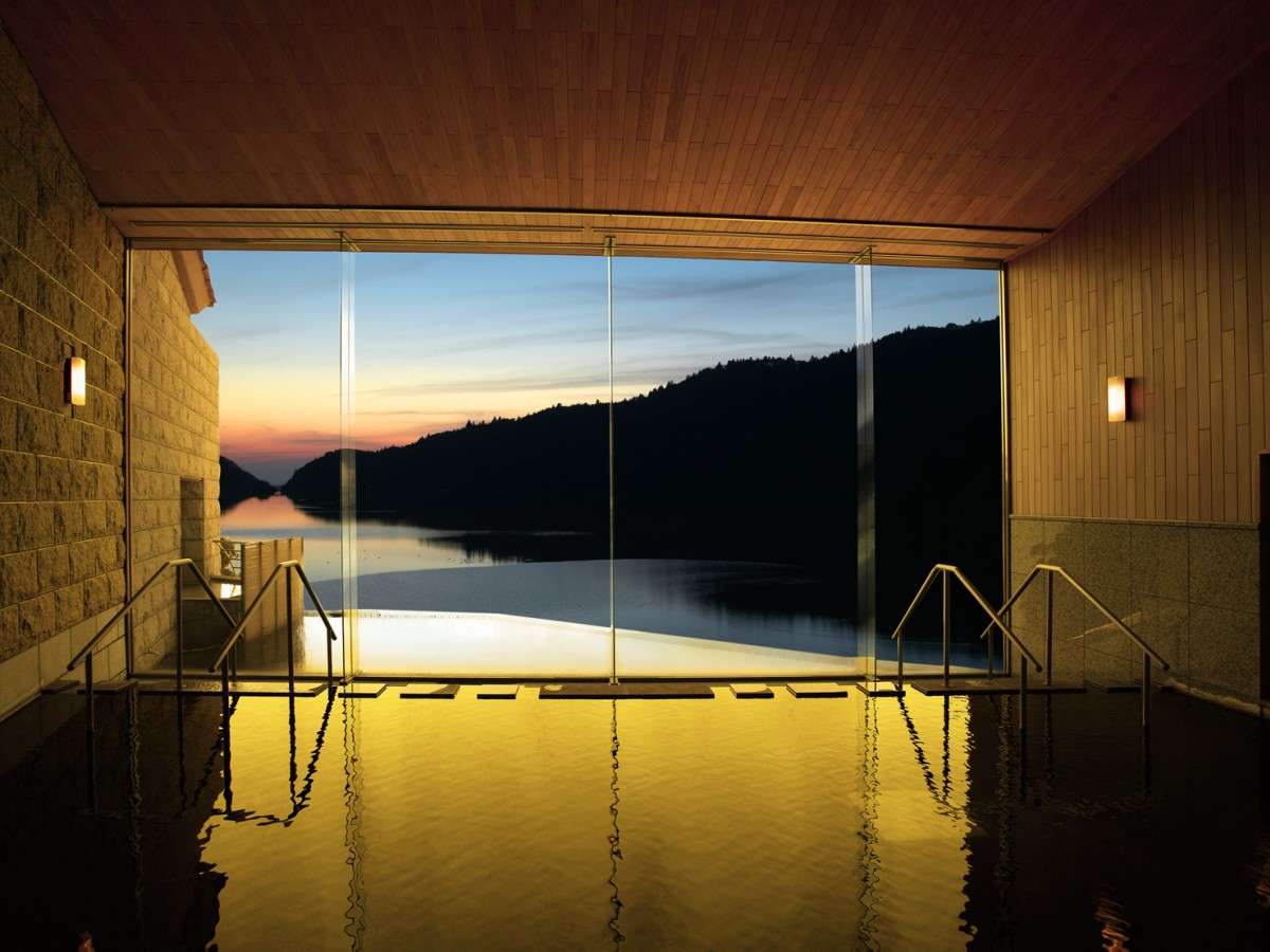 Indoor onsen bath at Unzen Azumaen with floor-to-ceiling windows facing the lake at sunset