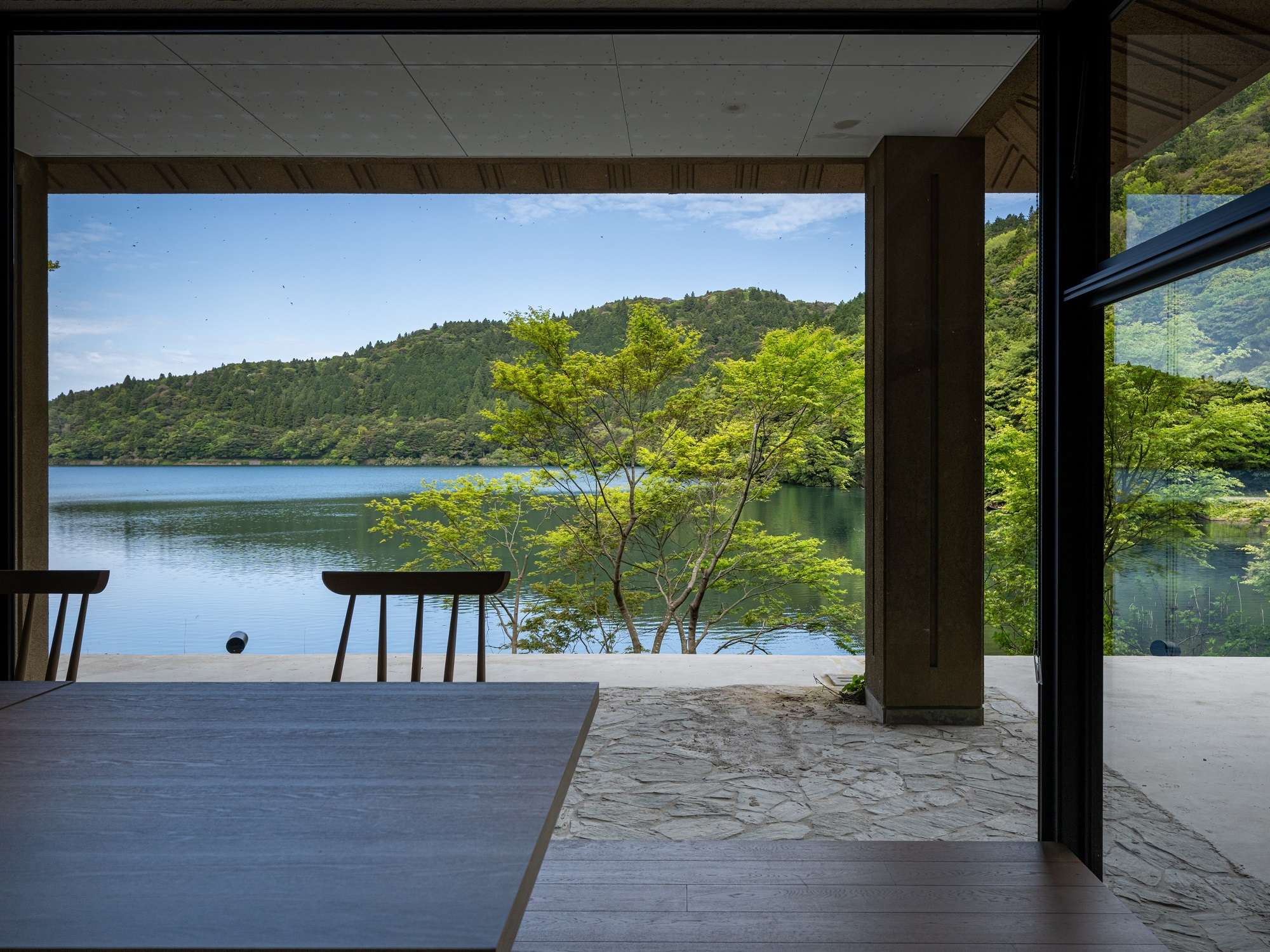 Lounge seating at Unzen Azumaen opening onto a stone terrace and calm lake through wide sliding doors