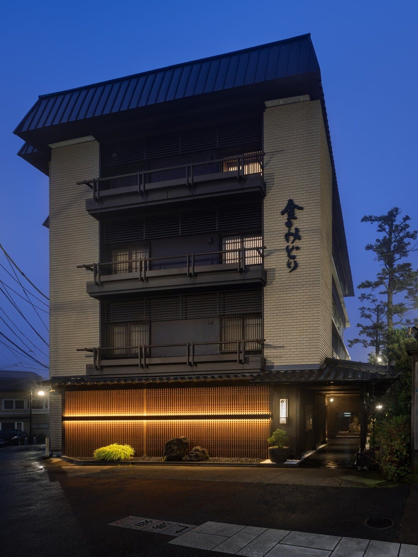 Mukashigokoro no Yado Kanemidori four-story building exterior at dusk with vertical signage and warm-lit lattice entrance in Kusatsu Onsen