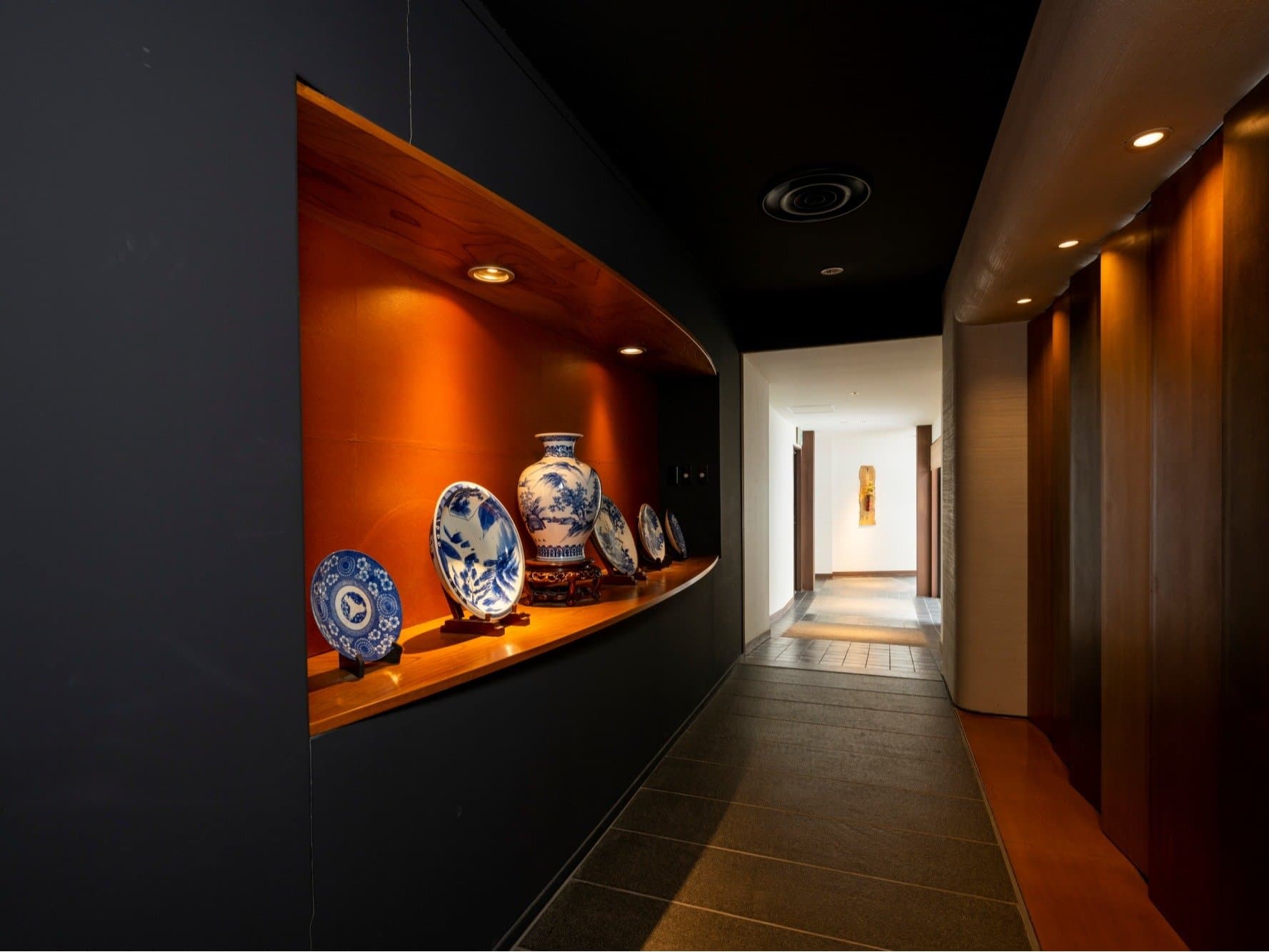 Dark corridor with lit alcove displaying blue-and-white porcelain plates and vase at Kanemidori