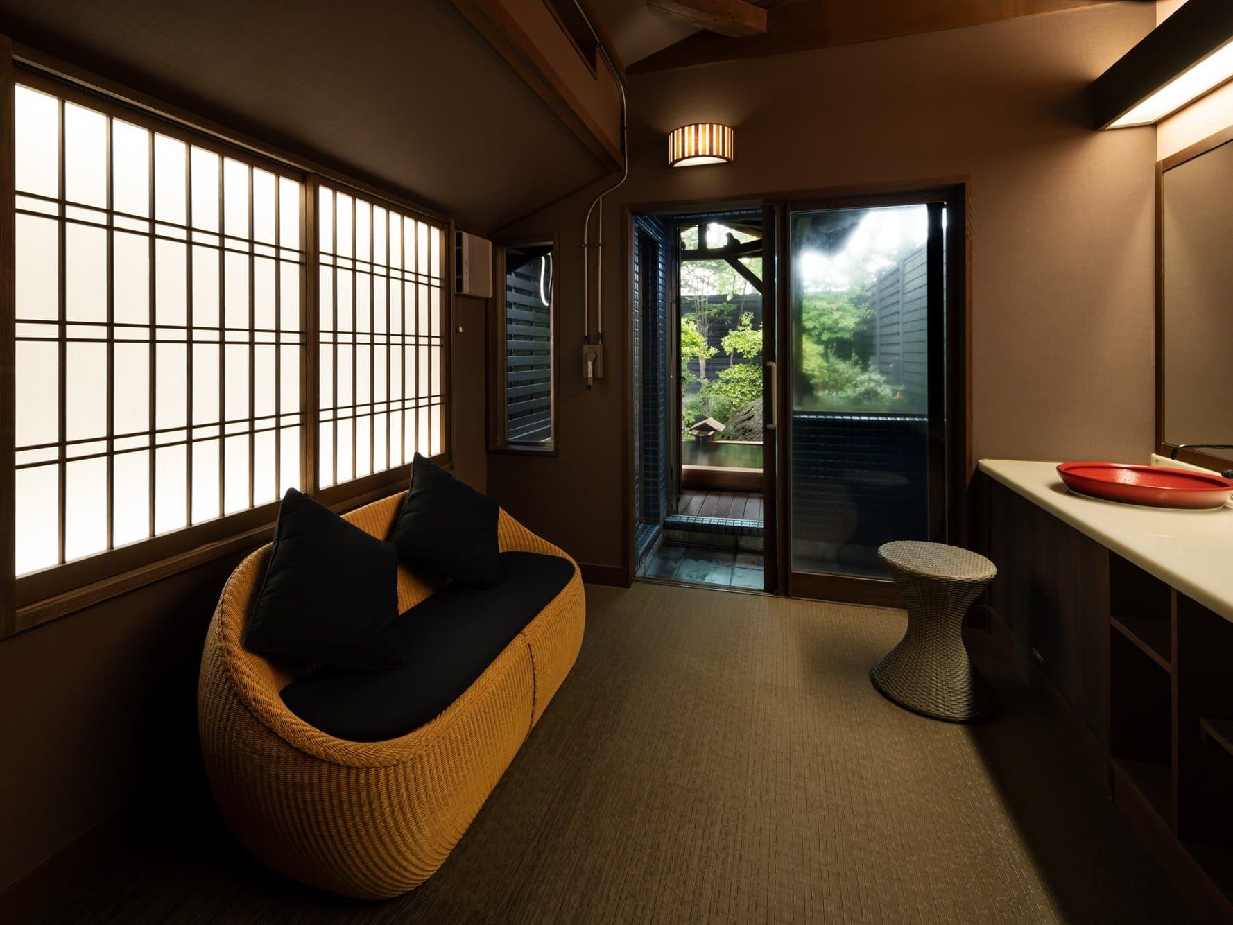 Private-bath relaxation anteroom with rattan sofa and shoji windows opening to the garden bath at Kanemidori