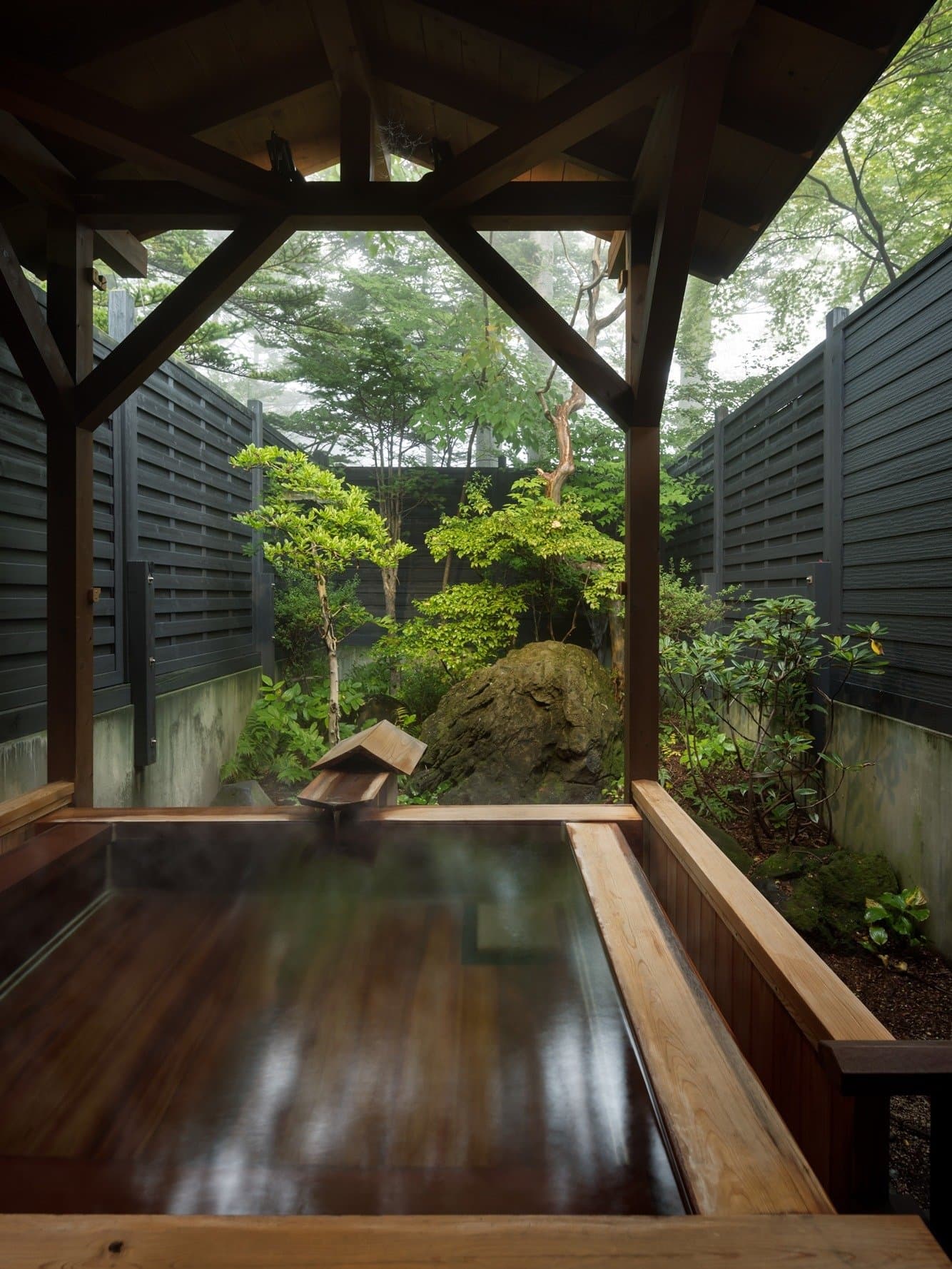 Roofed wooden open-air private bath looking onto a fenced garden at Kanemidori