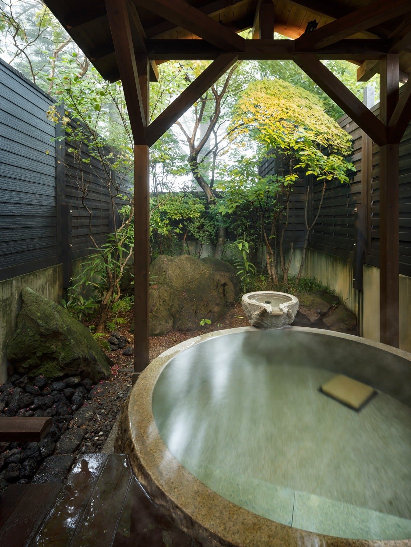 Stone outdoor rotenburo bath with rising steam framed by maple and garden greenery at Kanemidori