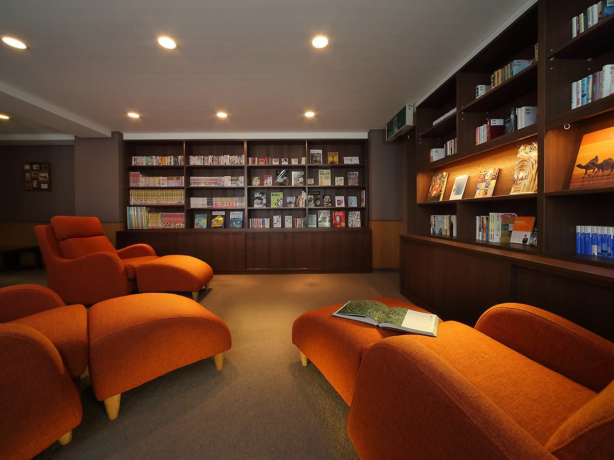 Library lounge at Hotel Tsuga no Ki with orange armchairs, footstools and wooden bookshelves filled with reading material