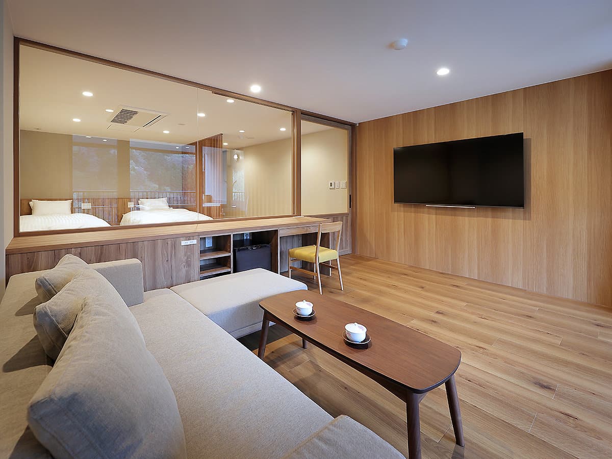 Modern Western-style guest room at Hotel Tsuga no Ki with twin beds behind a glass partition, sofa and wood-panelled lounge